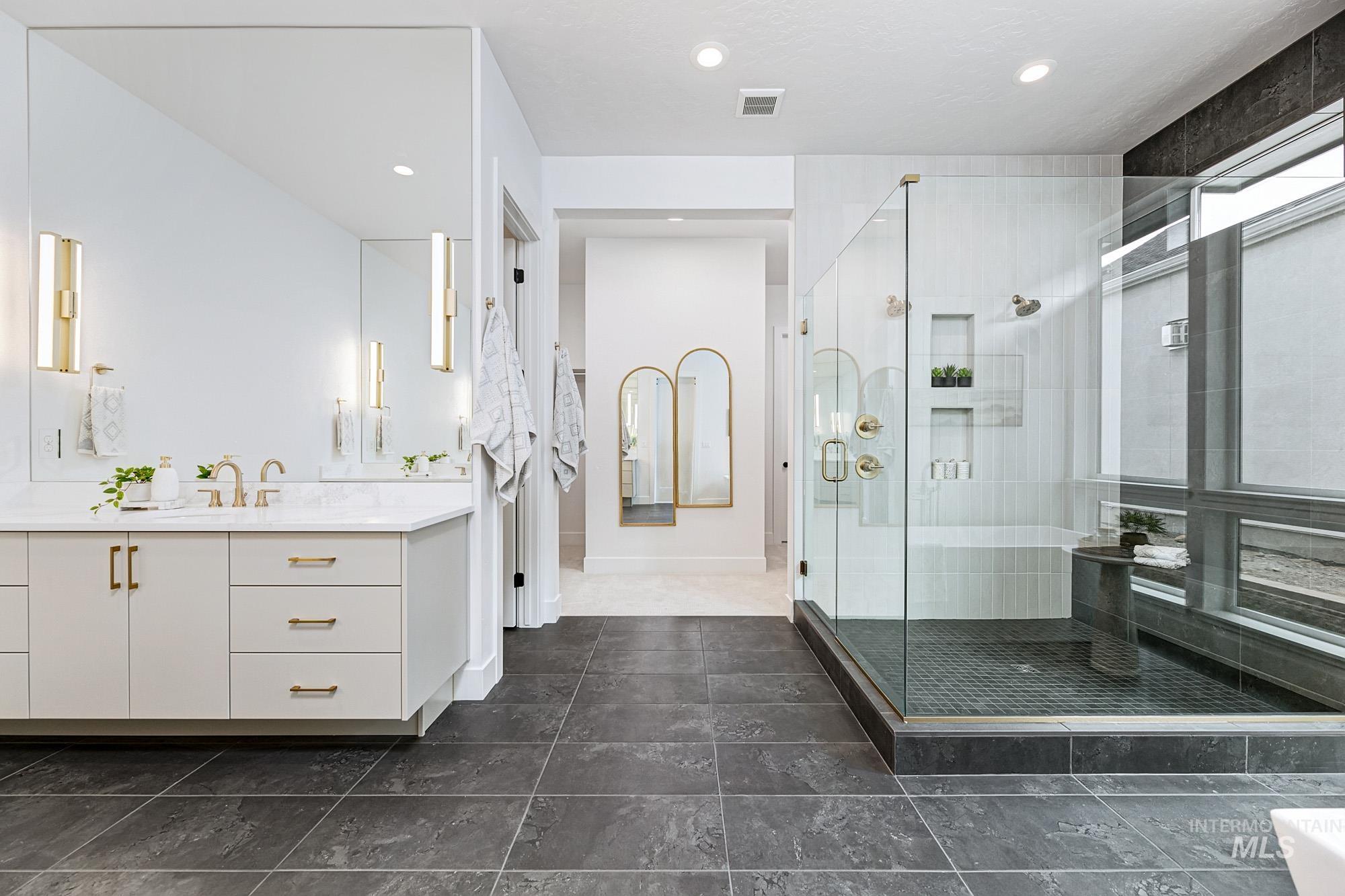 Modern bathroom featuring a dual vanity with white countertops, a spacious glass-enclosed shower, dark large-format floor tiles, and recessed lighting