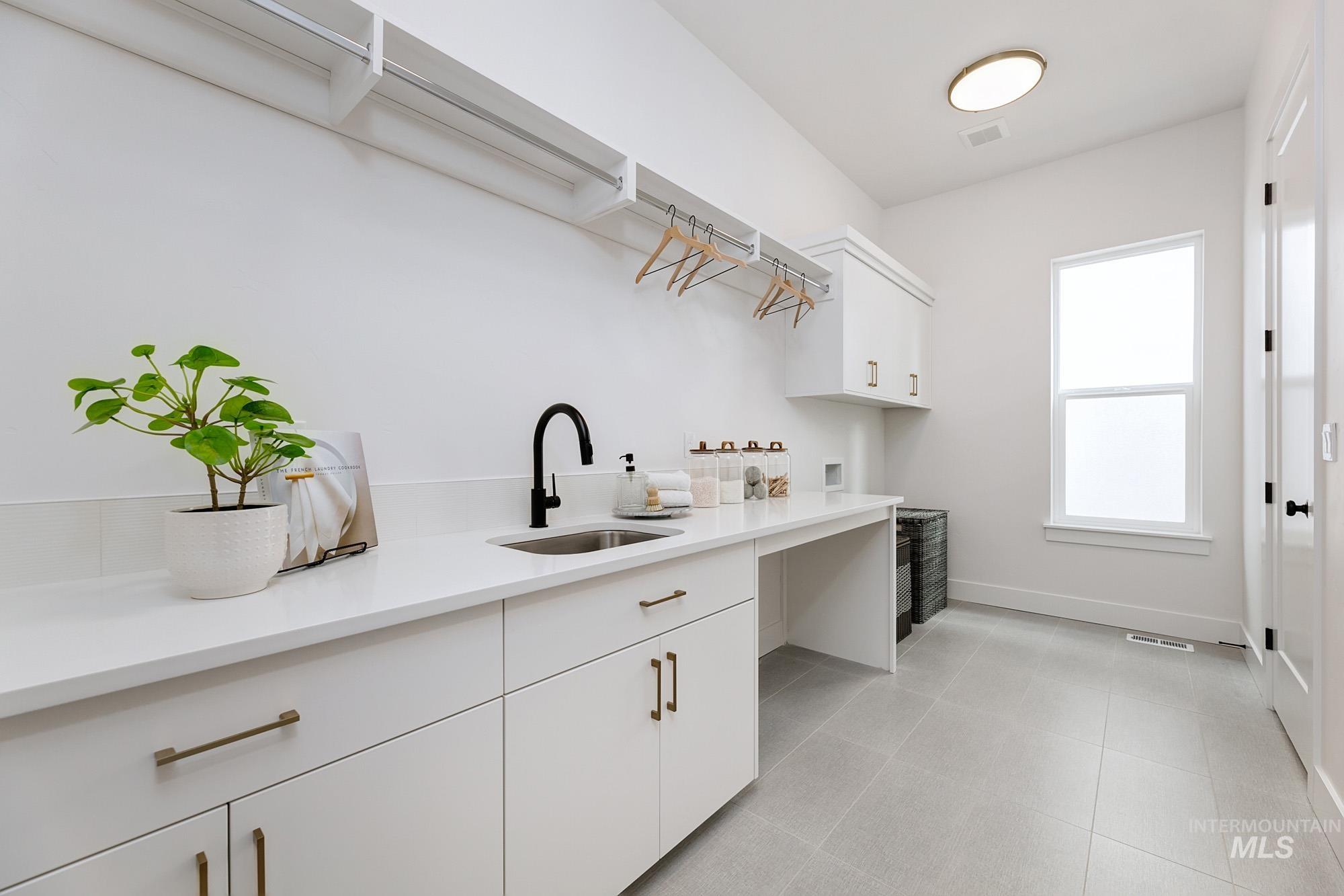 Laundry room featuring a deep basin sink with matte black faucet, extensive white cabinetry, integrated countertop space, and large format floor tiling