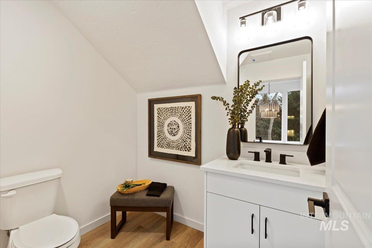 Half bath featuring vanity, light wood-style floors, and vaulted ceiling