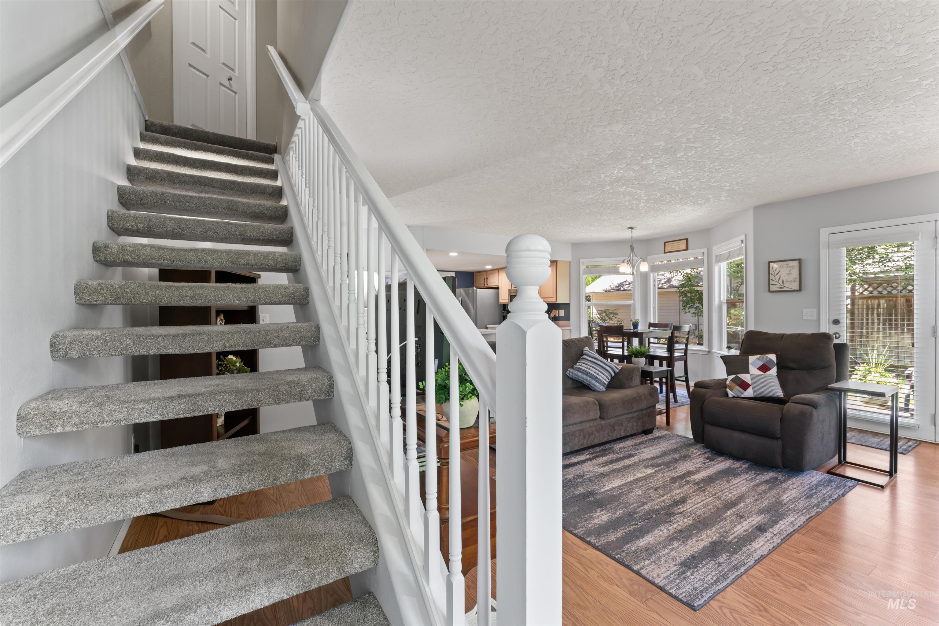 Staircase with plenty of natural light, wood finished floors, a textured ceiling, and a chandelier