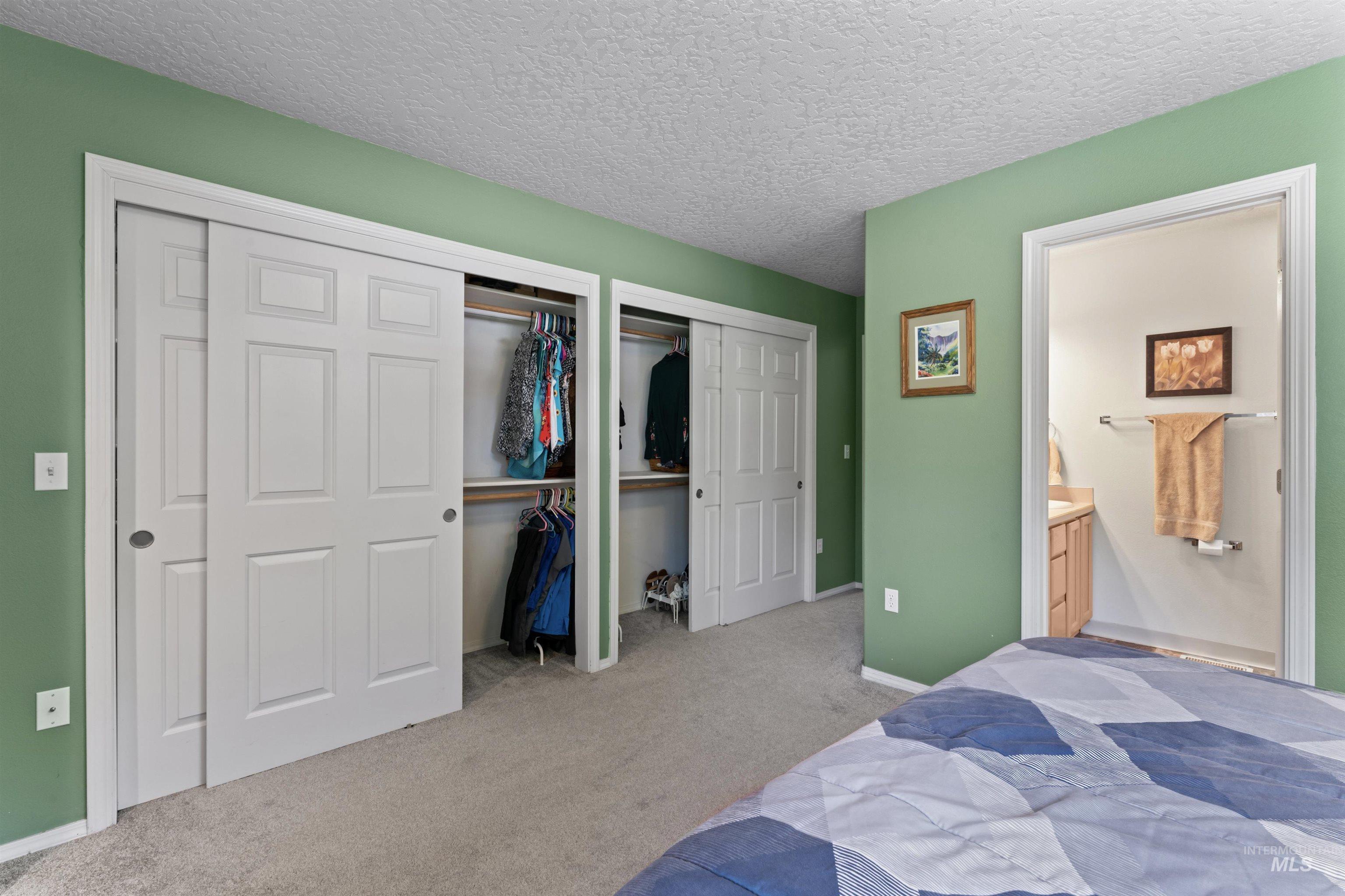 Carpeted bedroom featuring two closets, ensuite bathroom, and a textured ceiling