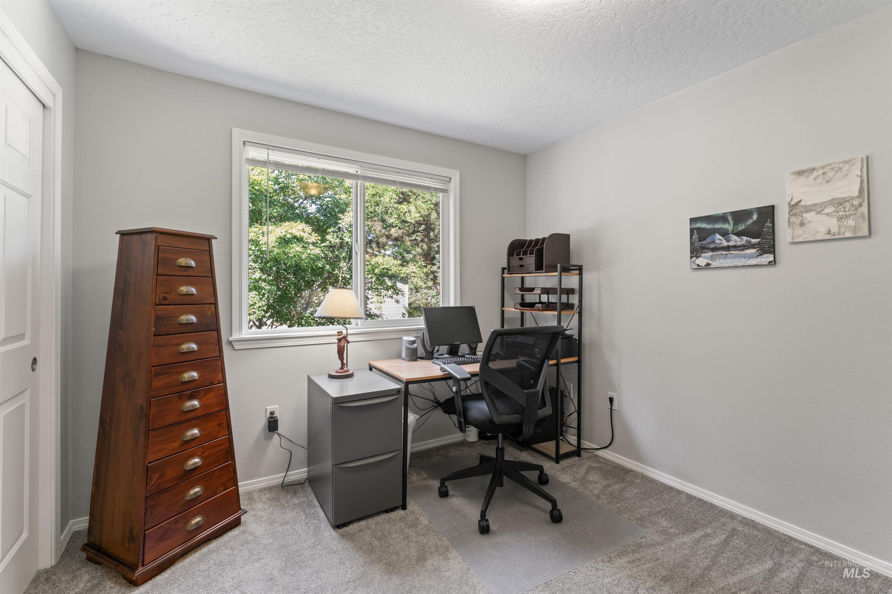 Carpeted office space featuring a textured ceiling and baseboards