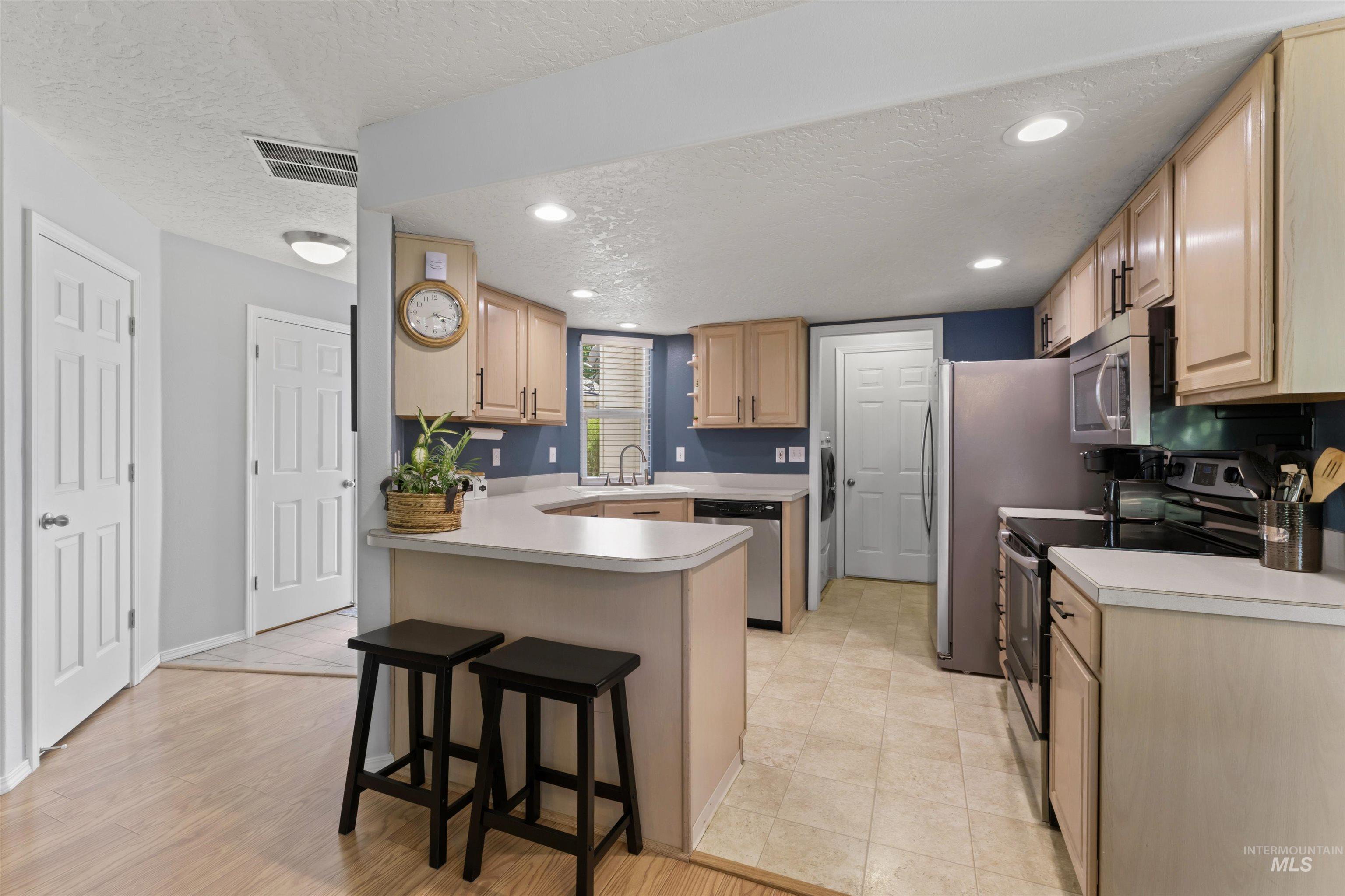Kitchen with appliances with stainless steel finishes, a peninsula, a textured ceiling, a breakfast bar, and light countertops