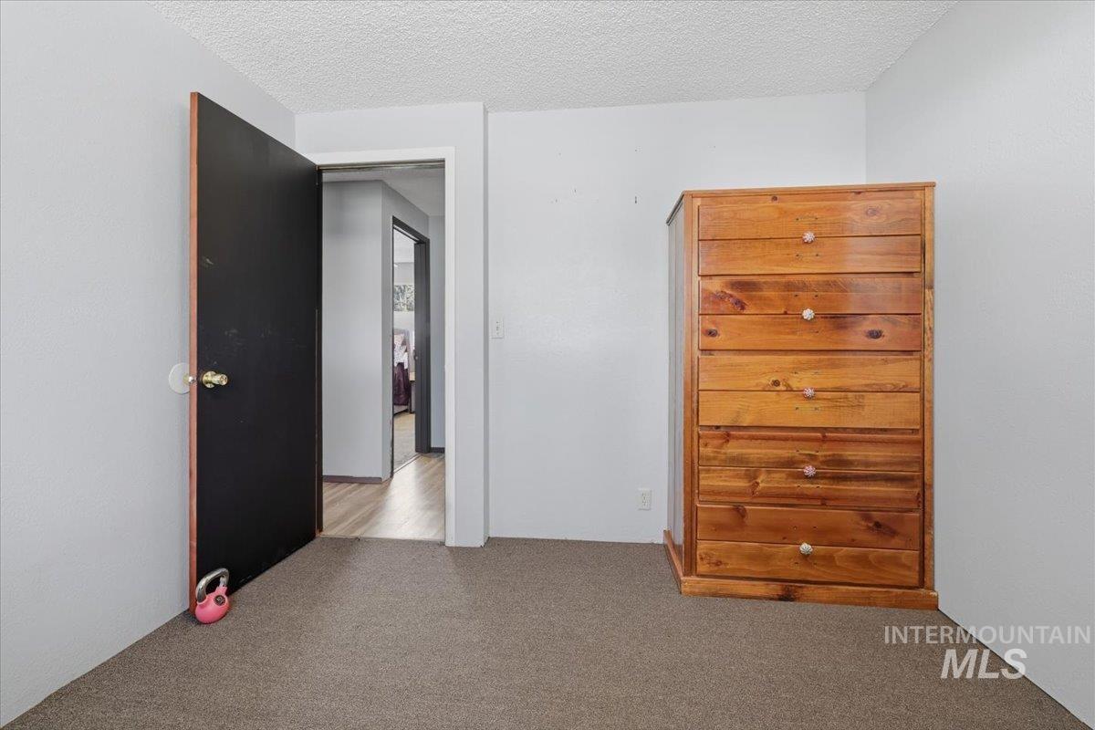 Carpeted room with light gray walls and a textured ceiling