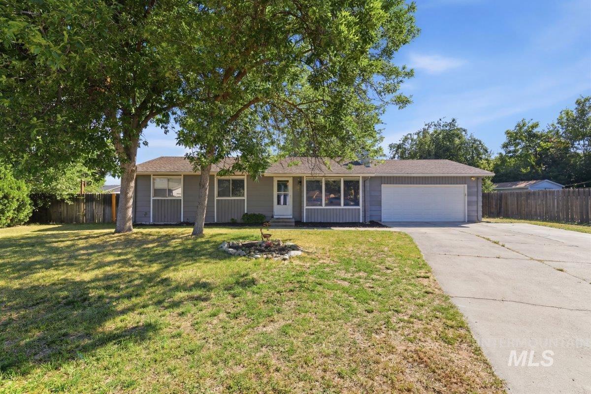 Single-story residence featuring a two-car garage, a concrete driveway, and a front lawn with mature trees