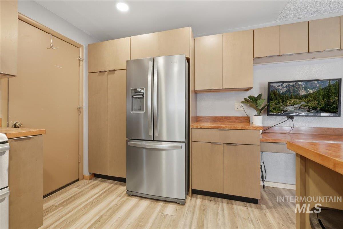 Kitchen featuring wood-finish flooring, light wood cabinetry, stainless steel refrigerator, and wood-finish countertops