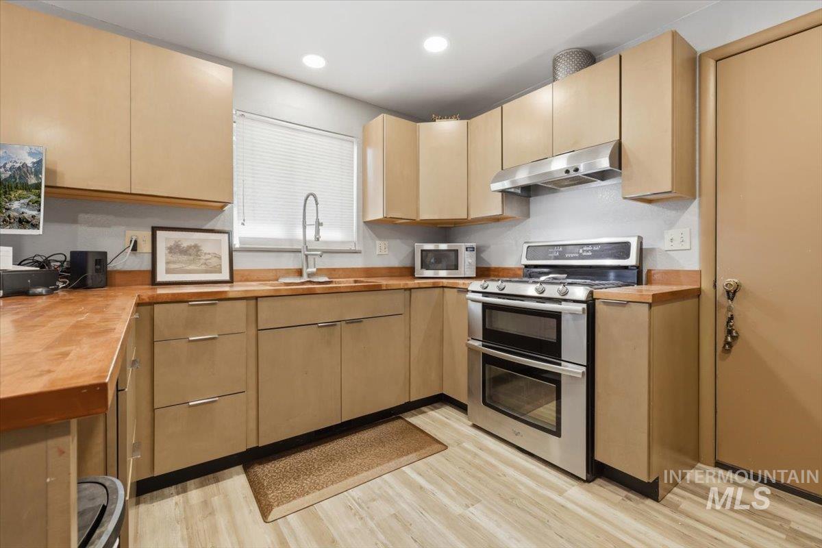 Kitchen featuring wood-finish countertops, stainless steel double oven range, stainless steel microwave, overhead cabinetry, and light wood-finish flooring