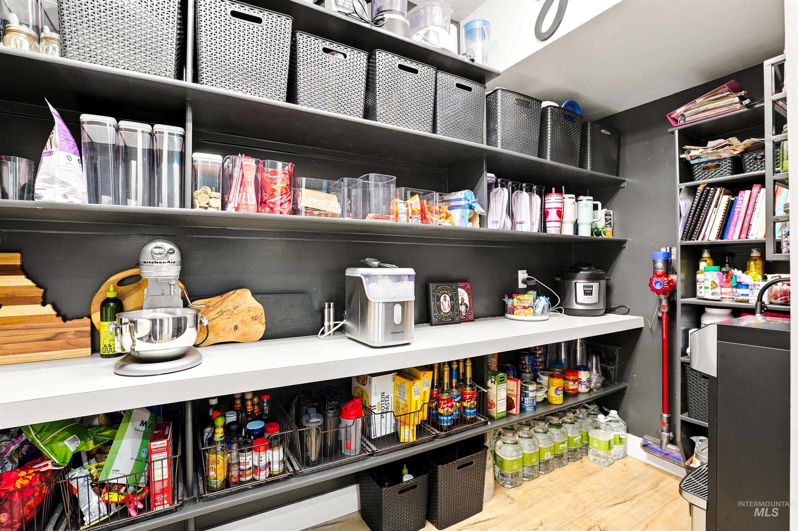 Built-in pantry shelving featuring light wood-finish flooring, dark wall paneling, and ample storage space