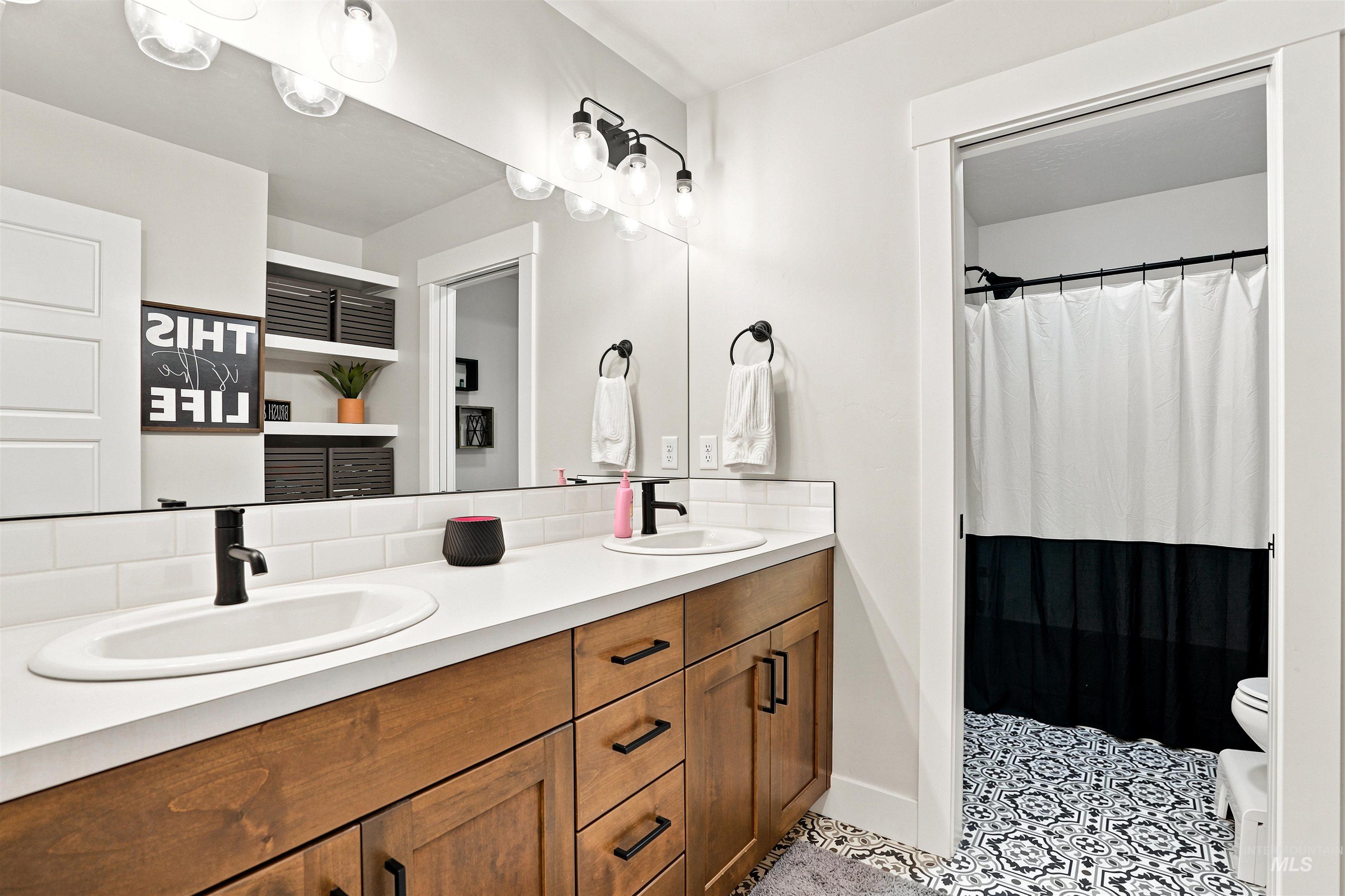 Double vanity with wood-finish cabinetry, white countertops, and matte black fixtures
