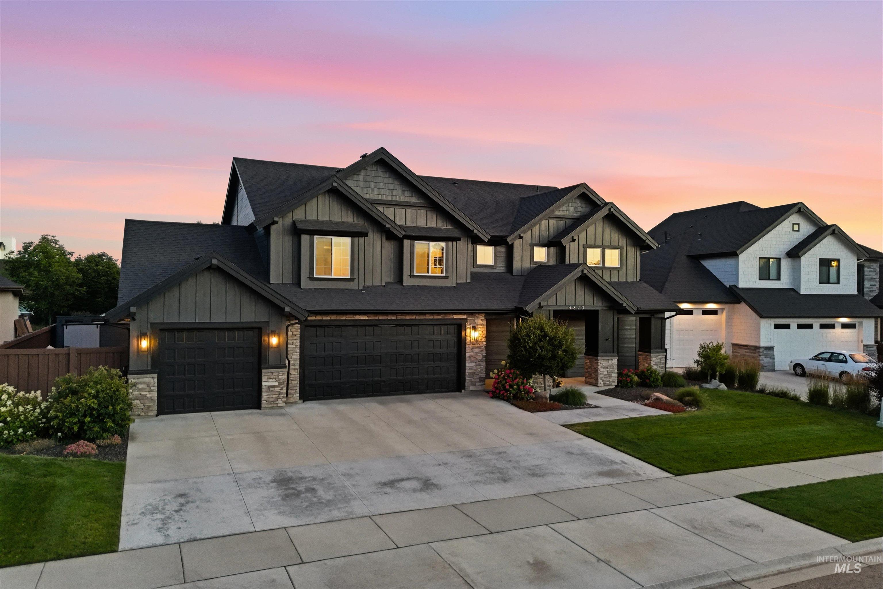 Contemporary residence featuring a dark gray exterior with vertical and horizontal siding, a multi-gabled roofline, stone accents, a three-car garage, and established front landscaping