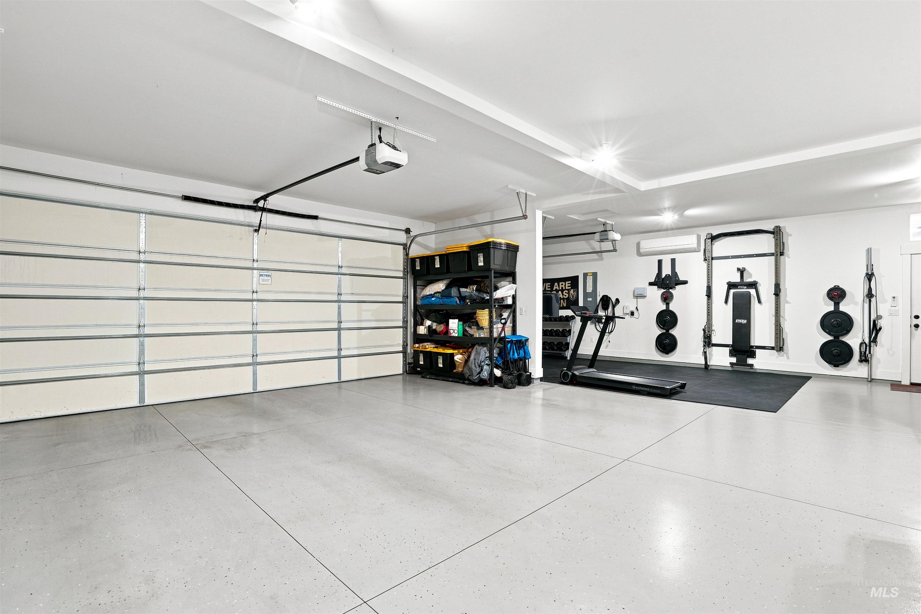 Spacious garage featuring a light-toned, durable flooring surface, multiple overhead lighting fixtures, and a prominent garage door