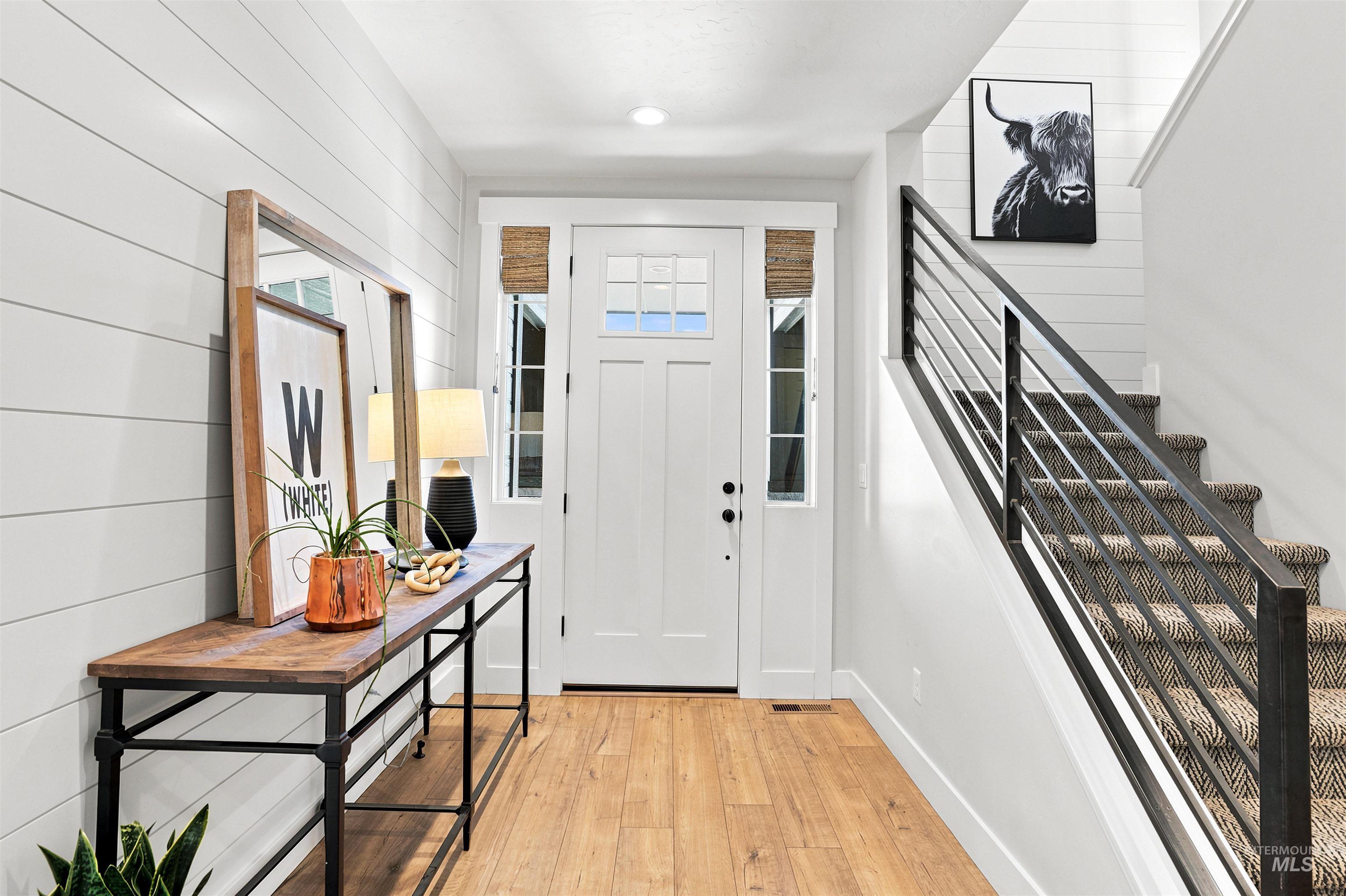 Entryway featuring a Craftsman-style front door with frosted glass panels, wood-finish flooring, shiplap accent wall, and a staircase with a modern metal railing and carpeted treads