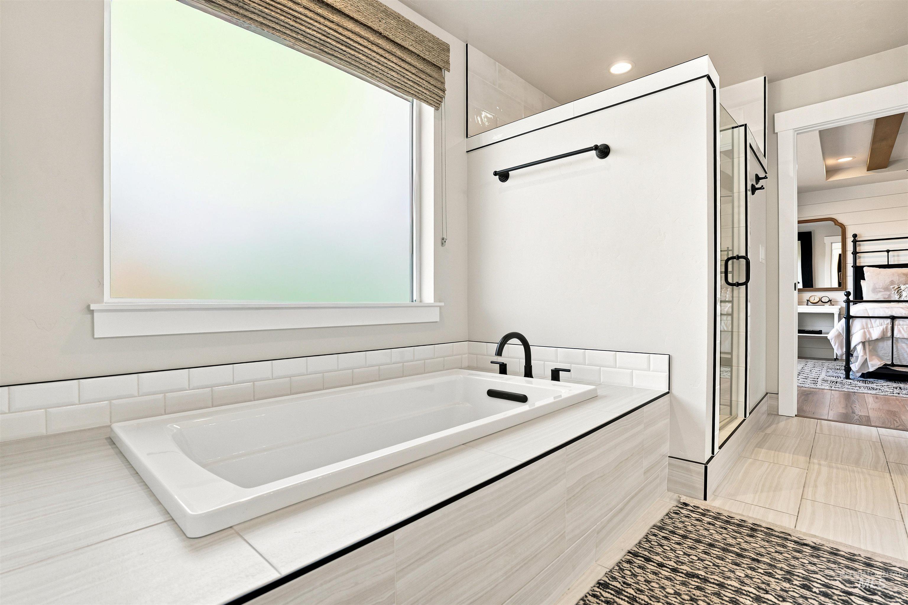 Soaking tub with matte black fixtures, surrounded by subway tile and wood-finish paneling