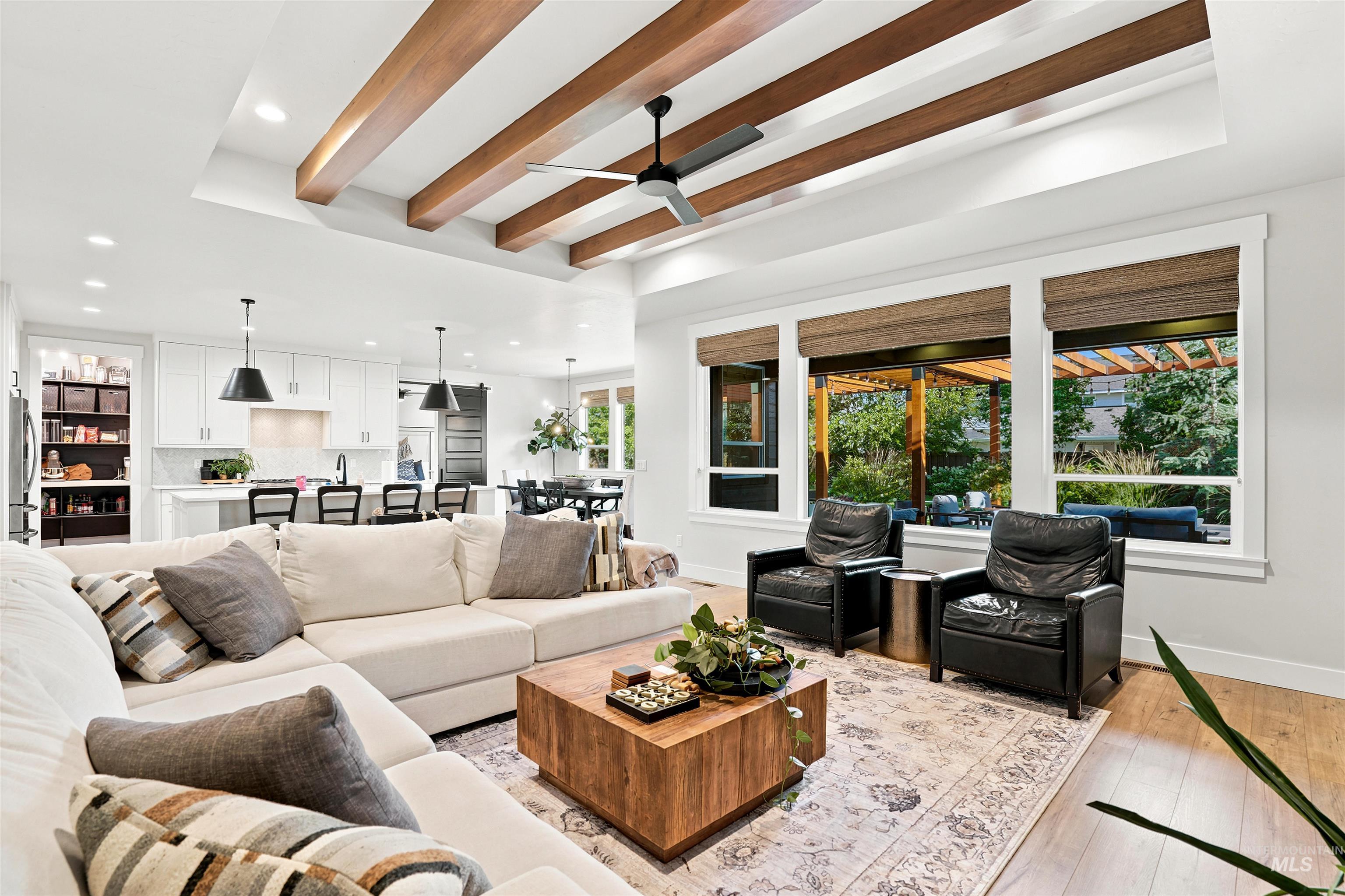 Open-concept living space with a tray ceiling featuring exposed wood beams and a ceiling fan