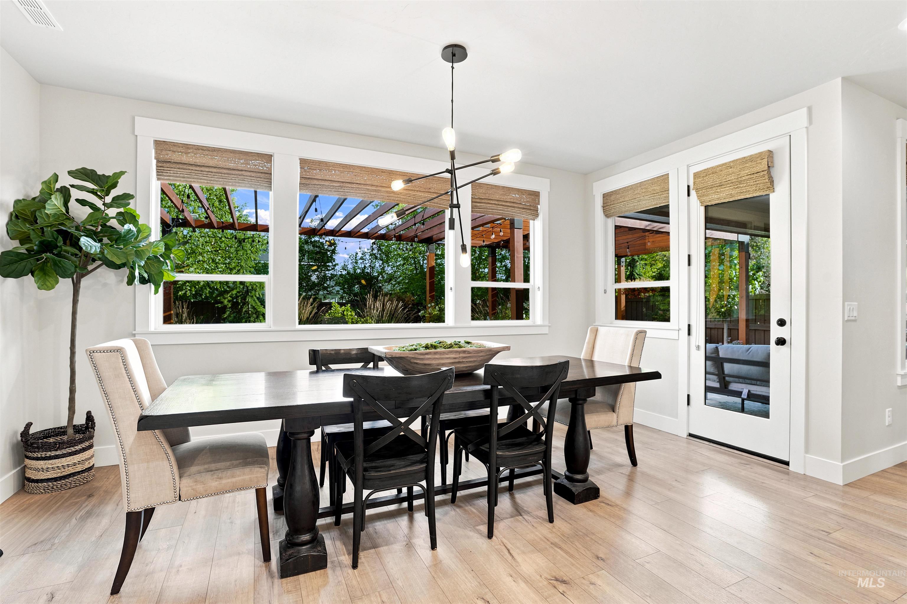 Dining area featuring light wood-finish flooring, multiple windows with woven blinds, and a glass-paneled door