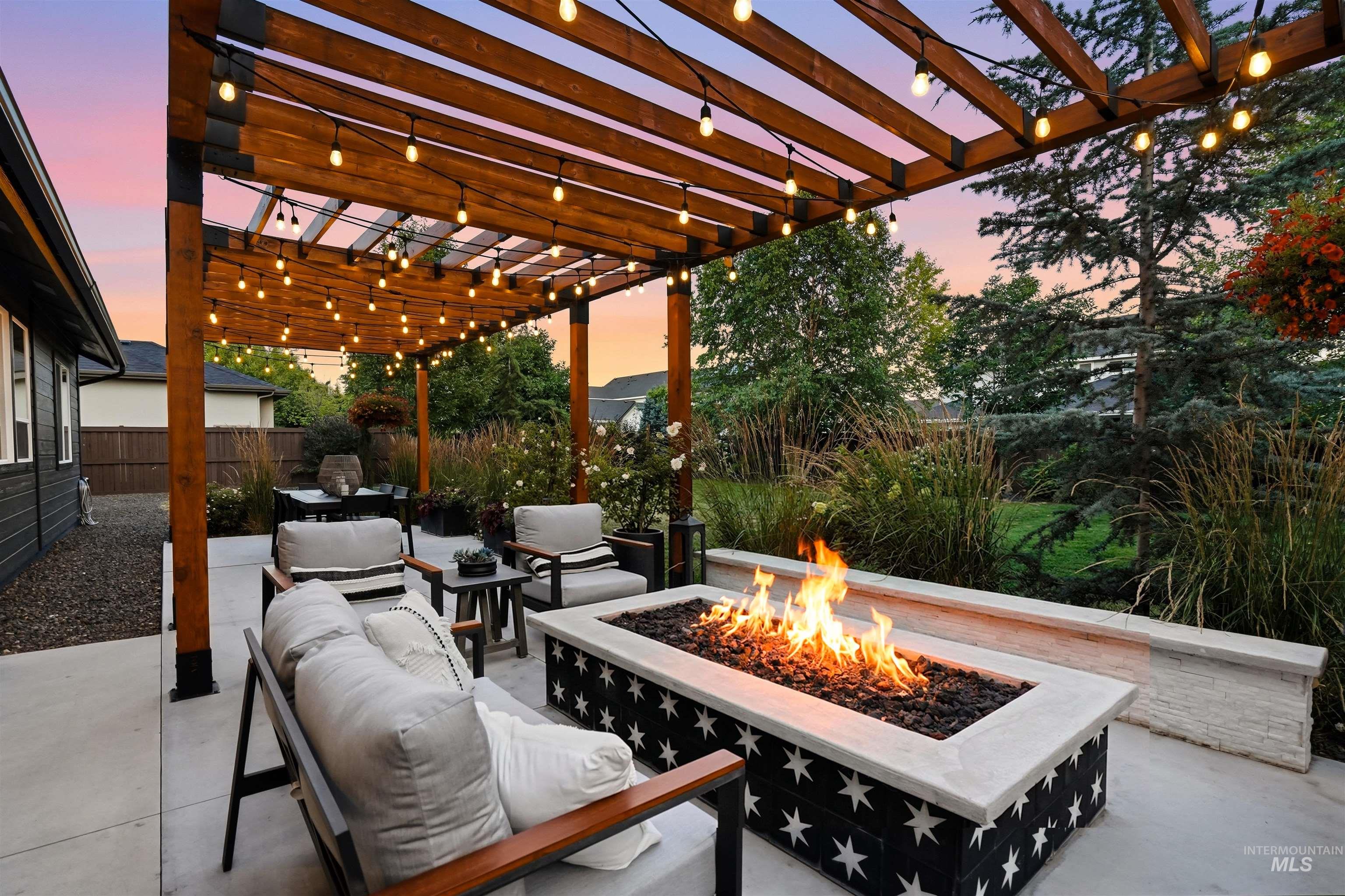 Outdoor patio featuring a custom wood pergola with string lighting, a built-in gas fire pit, and concrete hardscaping