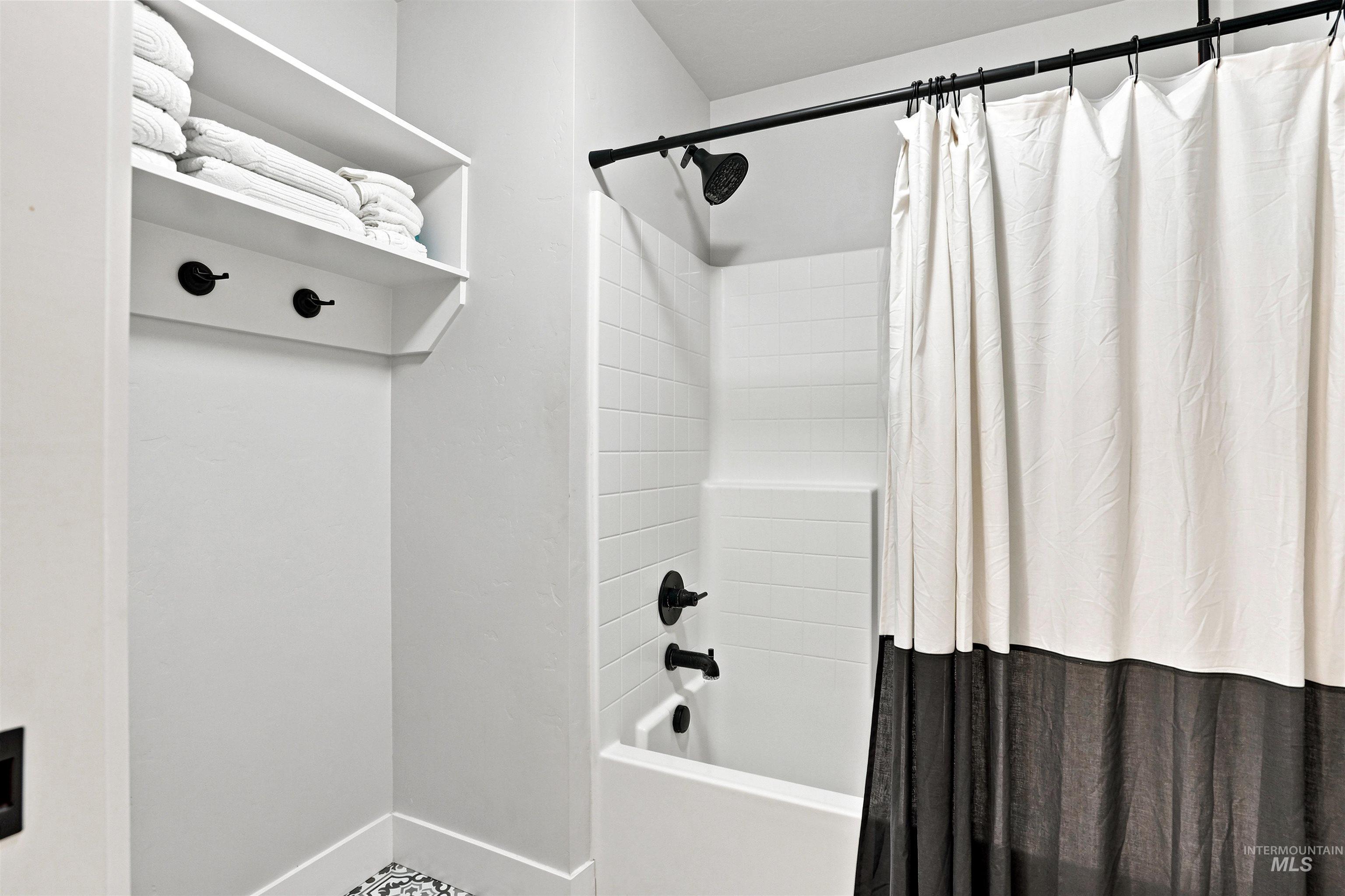 Bathroom featuring a clean white bathtub/shower combination with subway tile surround, dark bronze fixtures, and a built-in shelving unit with hooks
