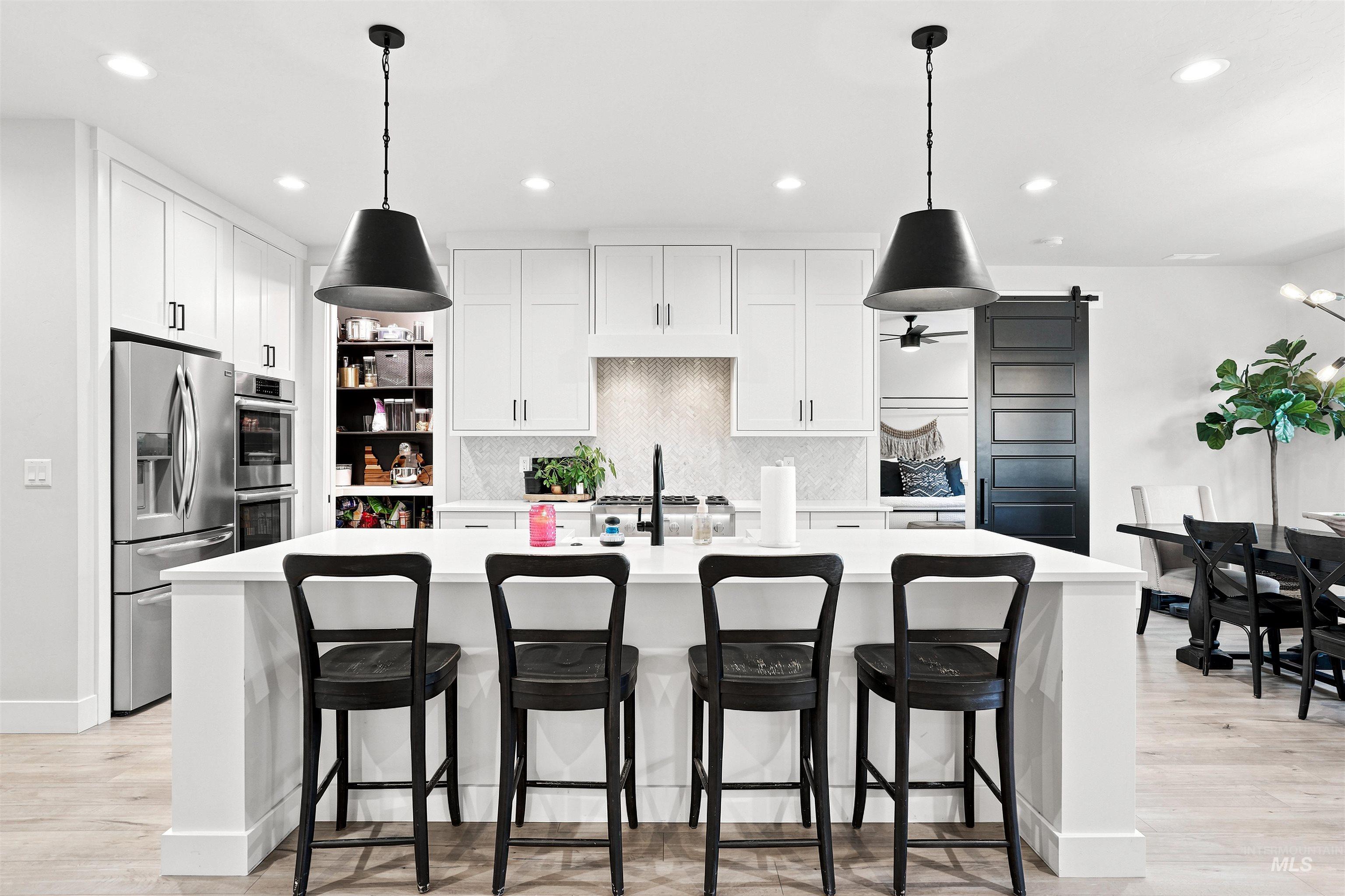 White kitchen featuring a large island with seating, stainless steel appliances, white cabinetry, a tiled backsplash, and recessed lighting