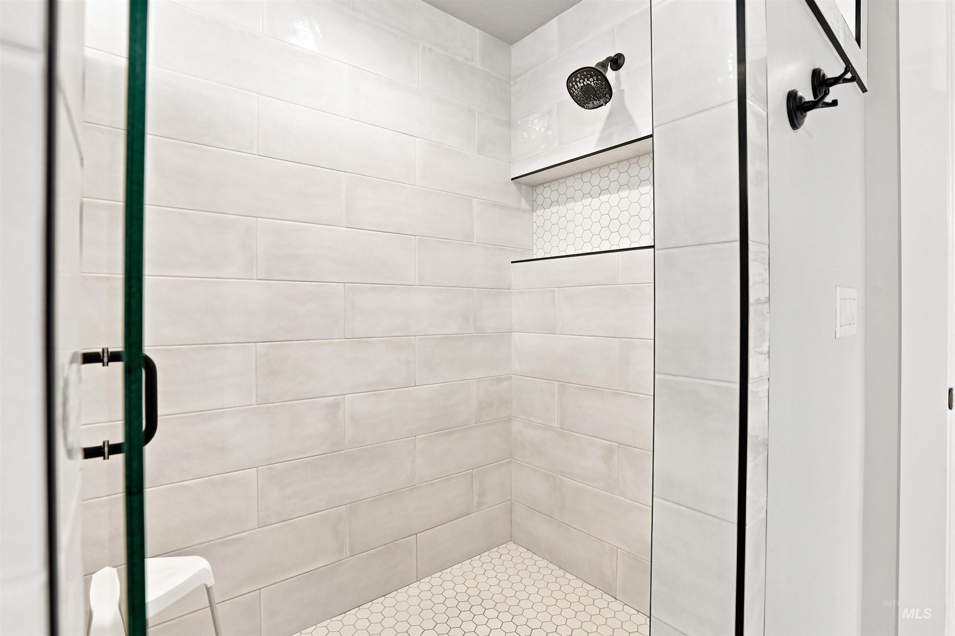 Glass-enclosed shower featuring large format tile walls and a hexagonal tile floor