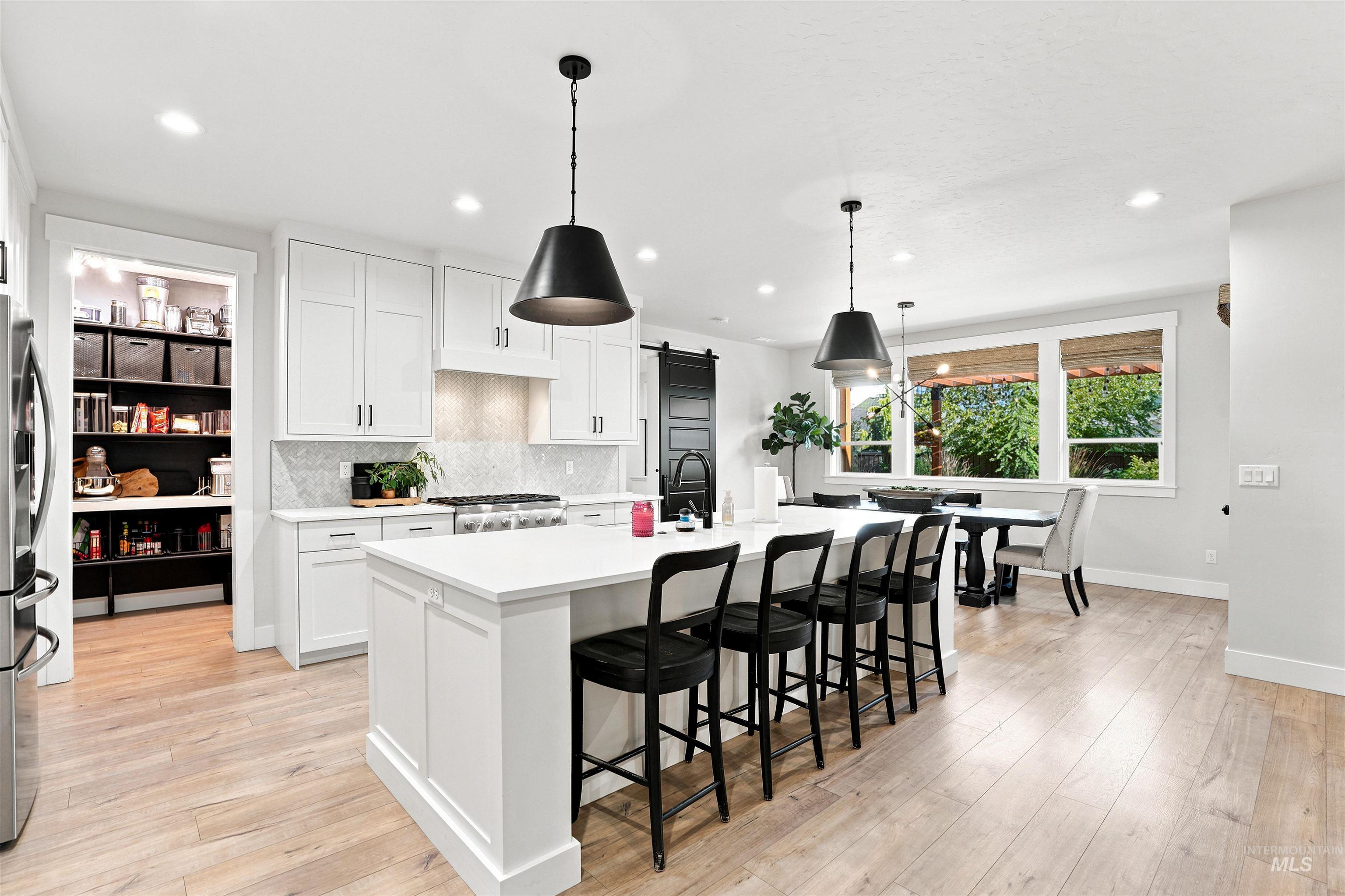 Kitchen featuring an expansive center island with seating, white shaker cabinetry, light wood-finish flooring, a patterned backsplash, and a pantry with built-in shelving