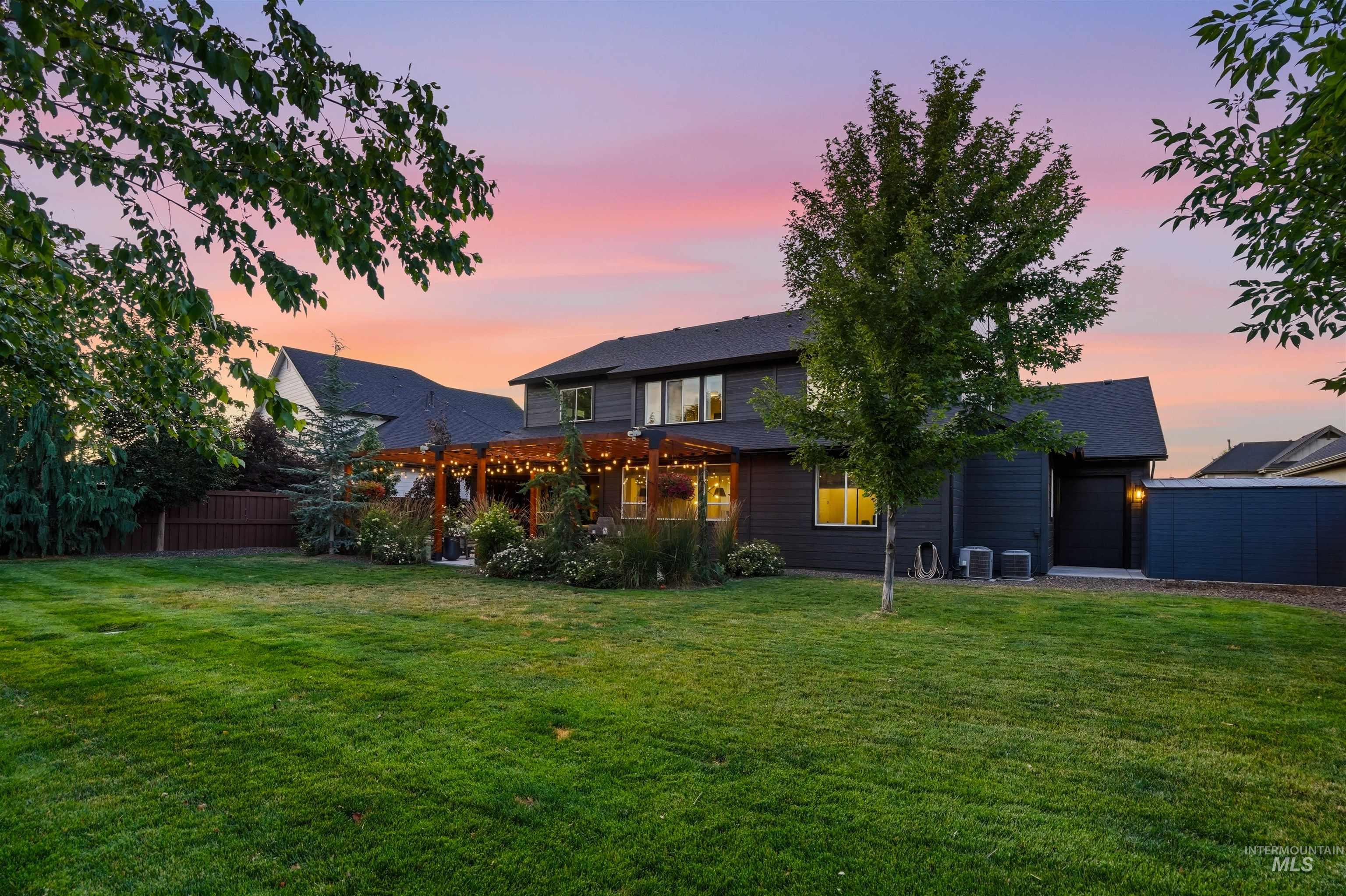 Expansive backyard featuring a lush lawn, mature trees, and a wooden pergola covering a patio area