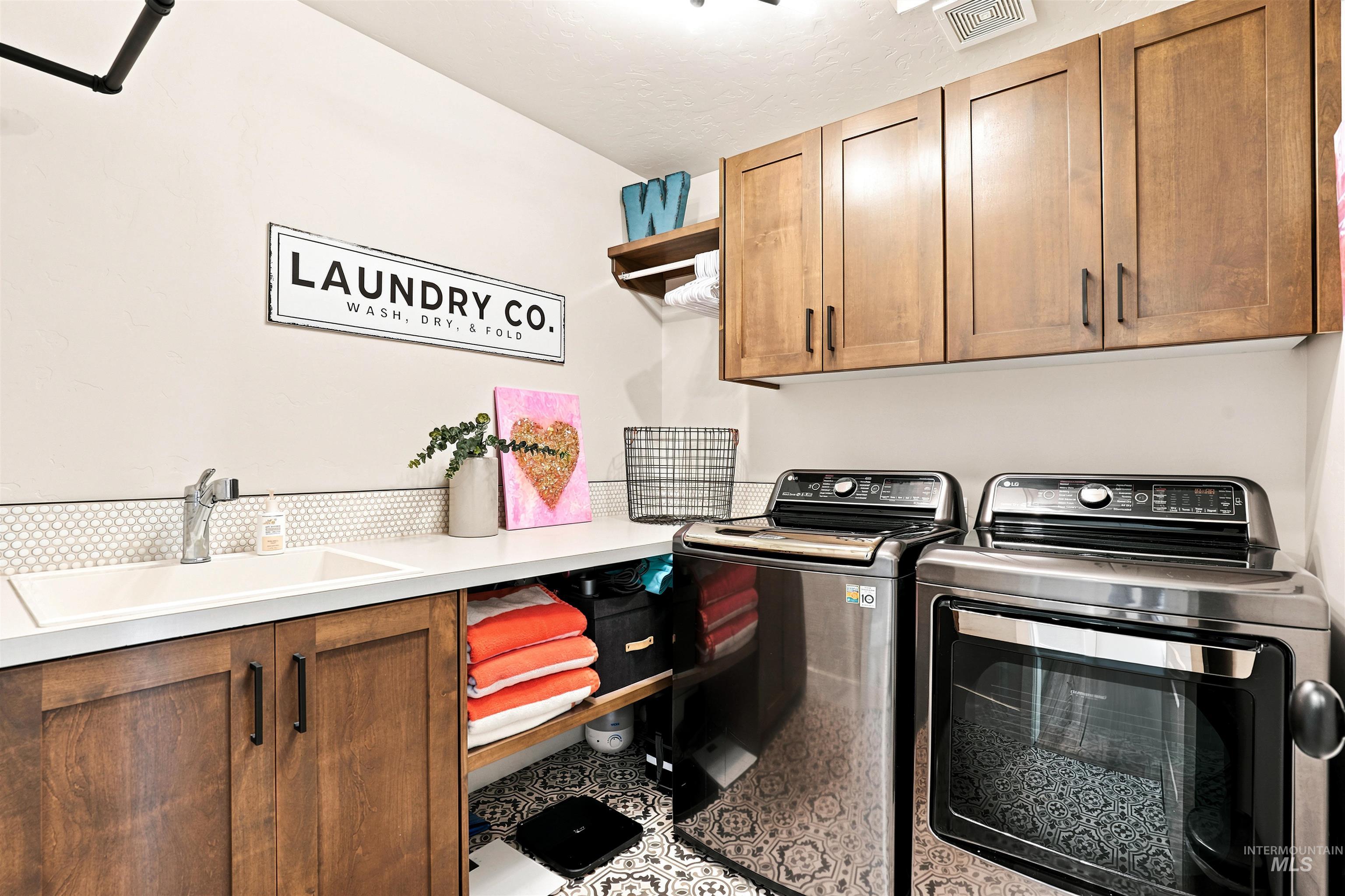 Laundry area featuring wood cabinetry with dark hardware, a built-in sink, and patterned floor tiling