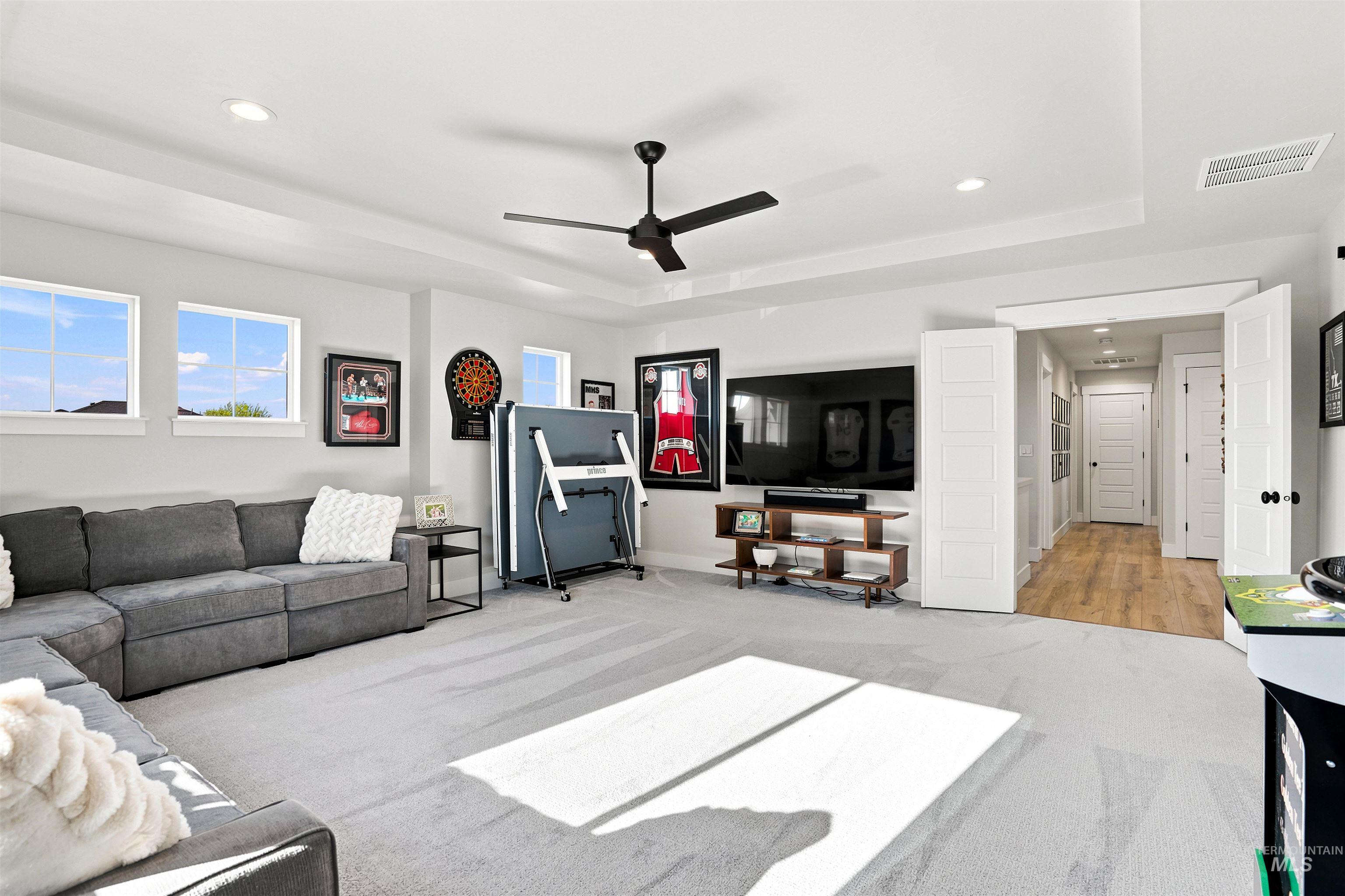 Spacious room featuring multiple windows, recessed lighting, a ceiling fan, tray ceiling detail, and carpet flooring