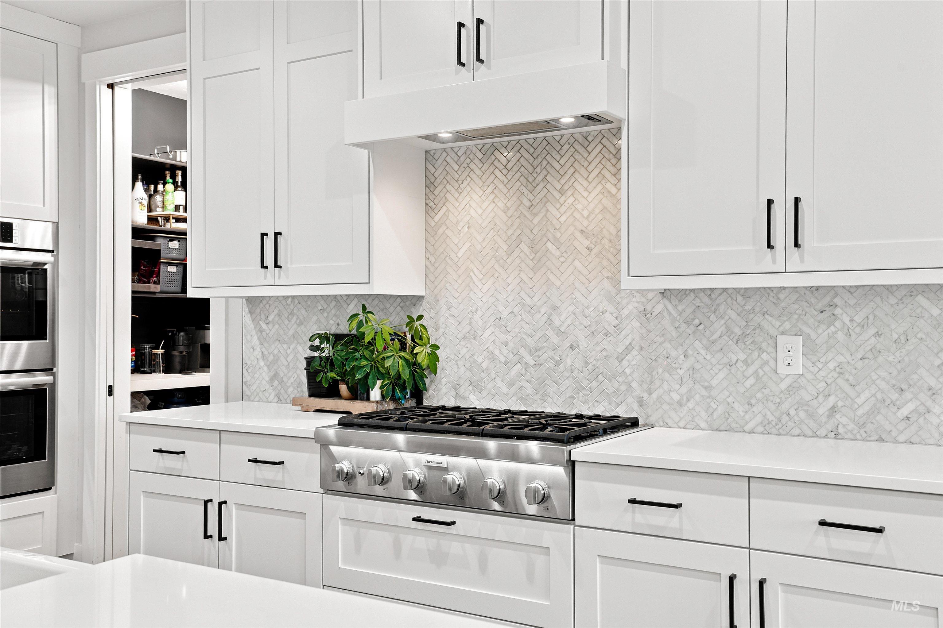 Kitchen featuring a stainless steel gas range, white shaker cabinetry with dark hardware, a herringbone pattern tile backsplash, and light-toned countertops