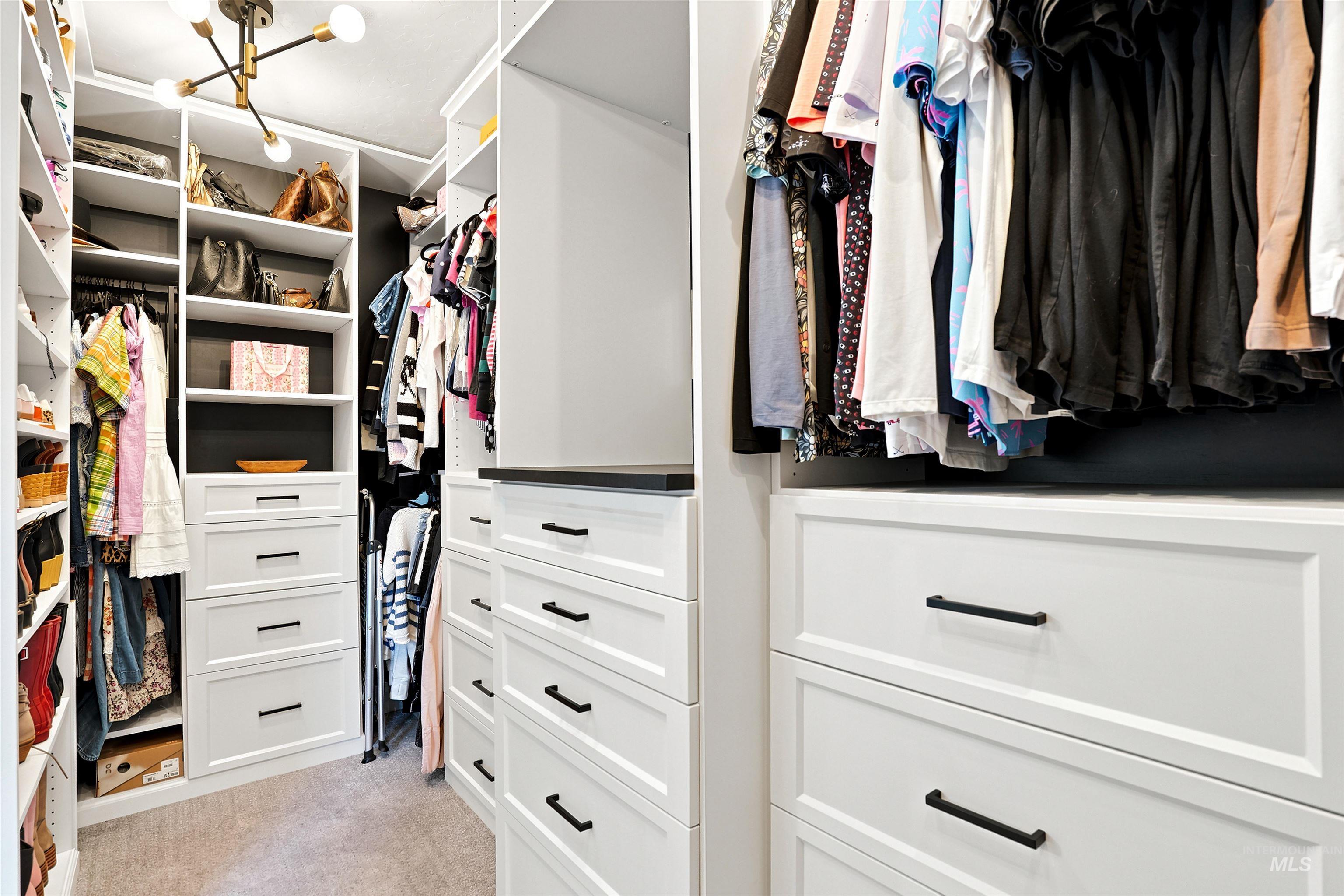 Custom closet system featuring white cabinetry, multiple hanging rods, integrated shelving, and built-in drawers with black hardware