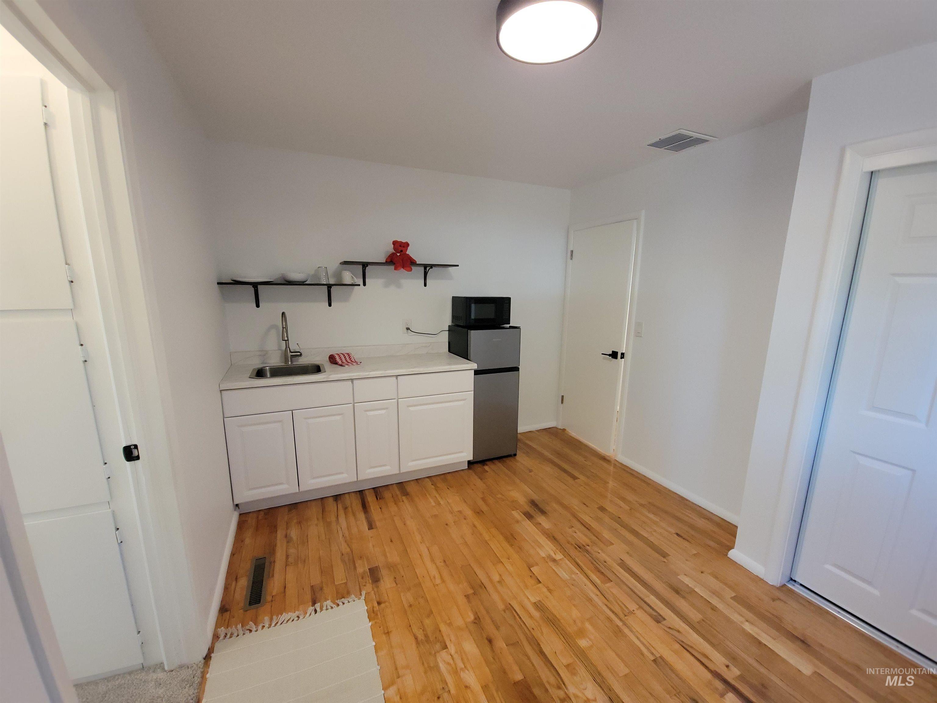 Kitchen with white cabinetry, light countertops, freestanding refrigerator, open shelves, and light wood-style floors