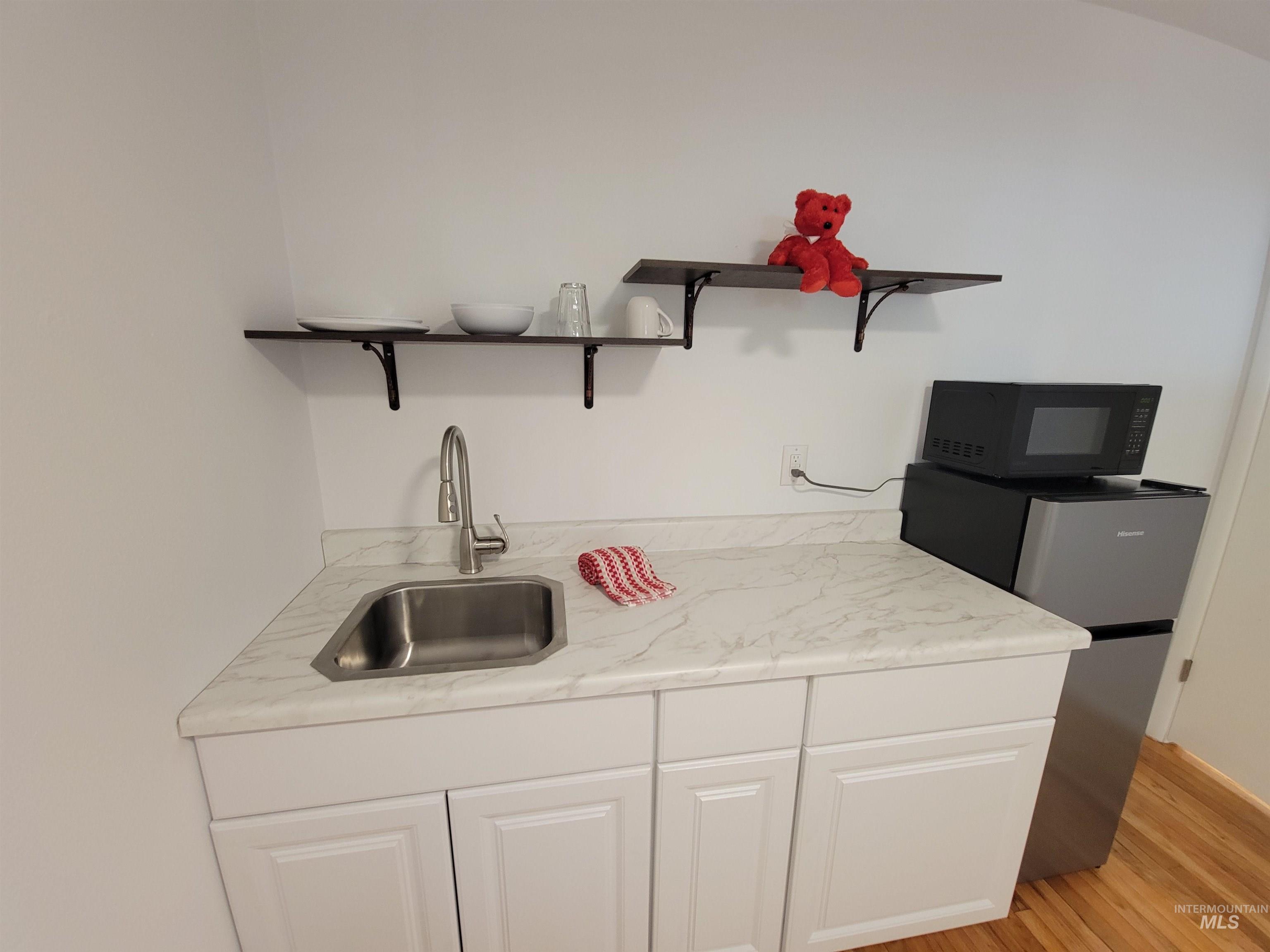 Kitchen featuring open shelves, white cabinetry, light wood finished floors, and black microwave