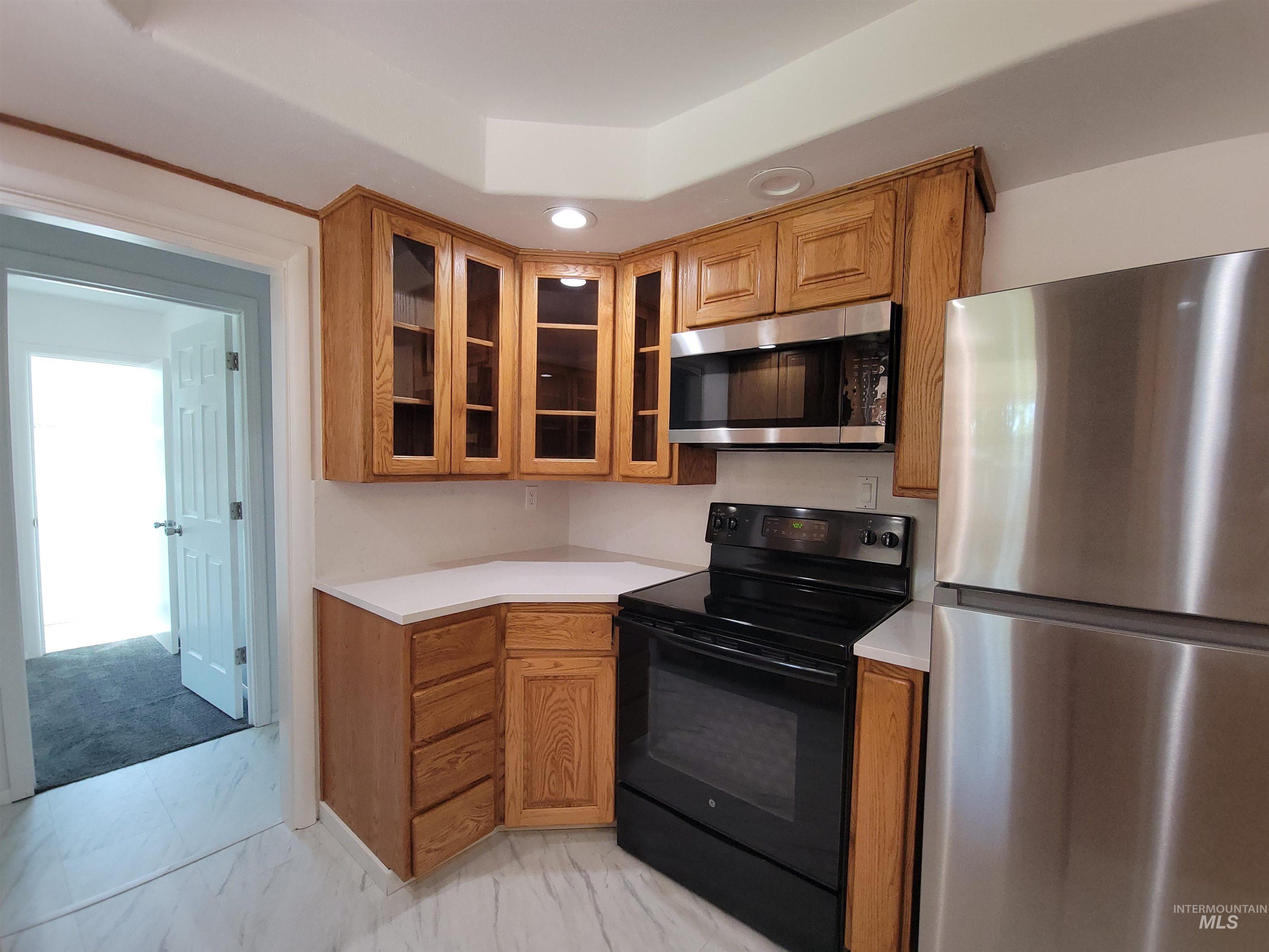Kitchen featuring appliances with stainless steel finishes, light countertops, light marble finish floors, brown cabinets, and glass insert cabinets