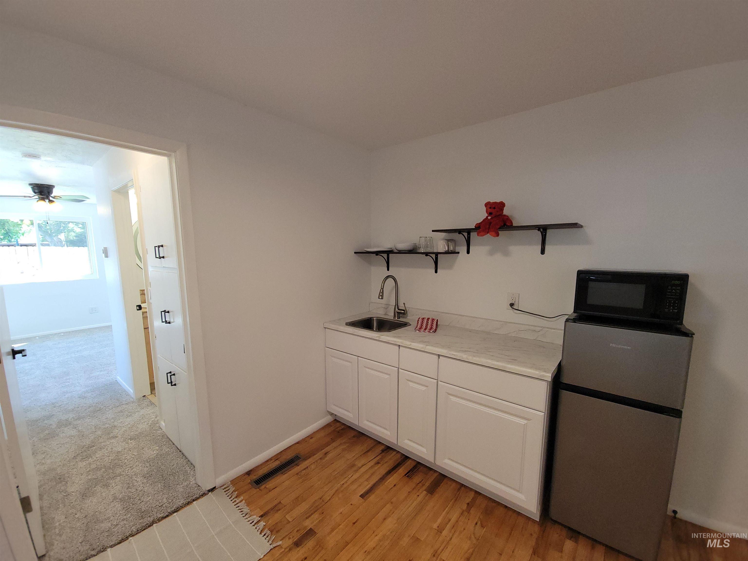 Bar area featuring white cabinets, refrigerator, open shelves, light countertops, and black microwave