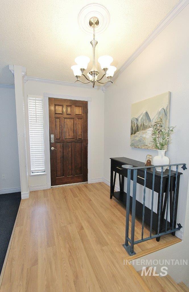 Foyer entrance featuring light wood-type flooring, a textured ceiling, crown molding, and a chandelier