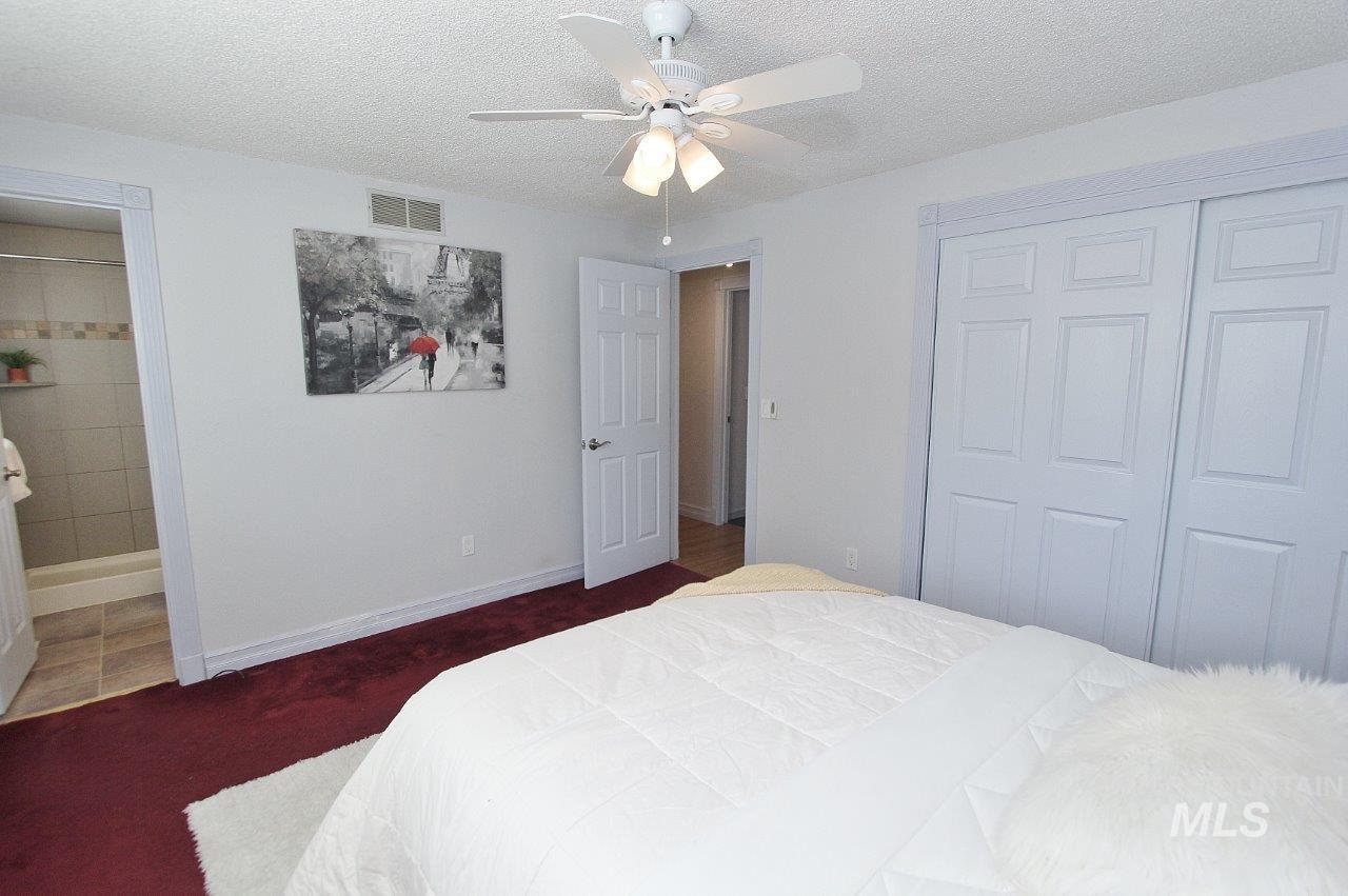 Carpeted bedroom featuring a textured ceiling, ceiling fan, ensuite bathroom, and a closet