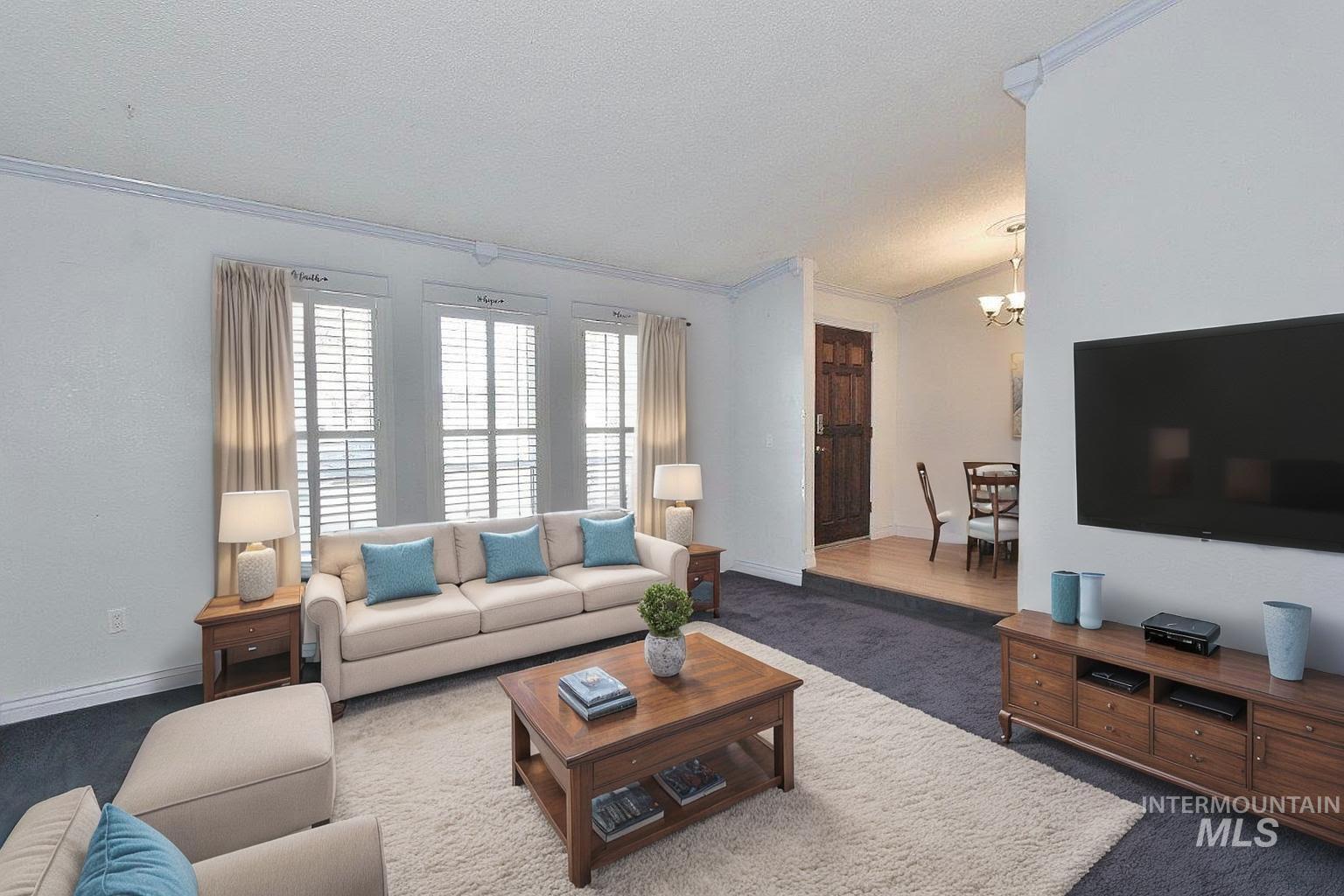 Living area featuring ornamental molding, carpet, a textured ceiling, and a chandelier