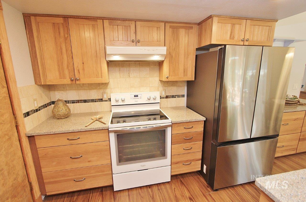 Kitchen with white range with electric stovetop, freestanding refrigerator, decorative backsplash, under cabinet range hood, and light brown cabinets