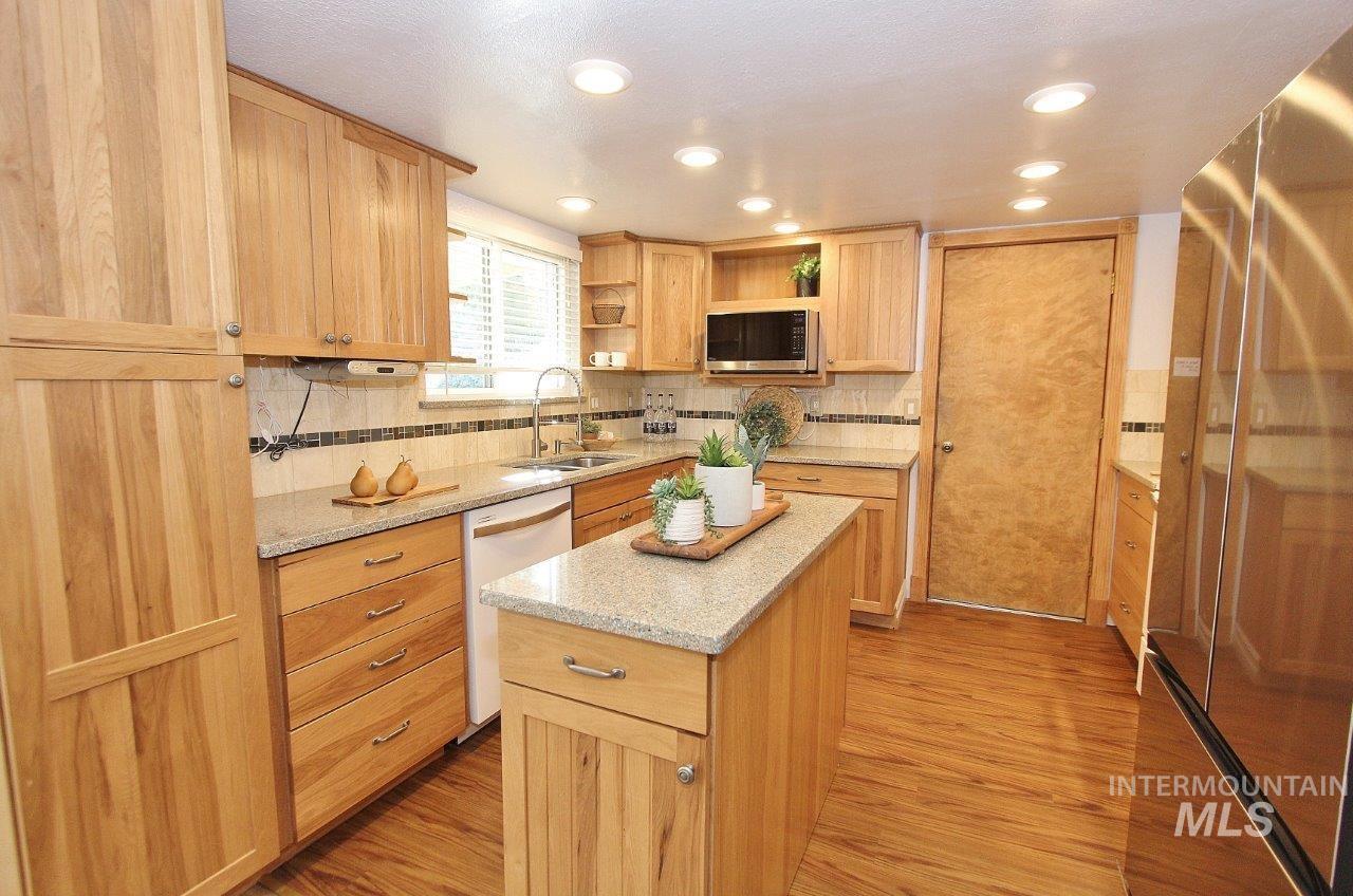 Kitchen with appliances with stainless steel finishes, tasteful backsplash, light brown cabinetry, light wood-type flooring, and recessed lighting