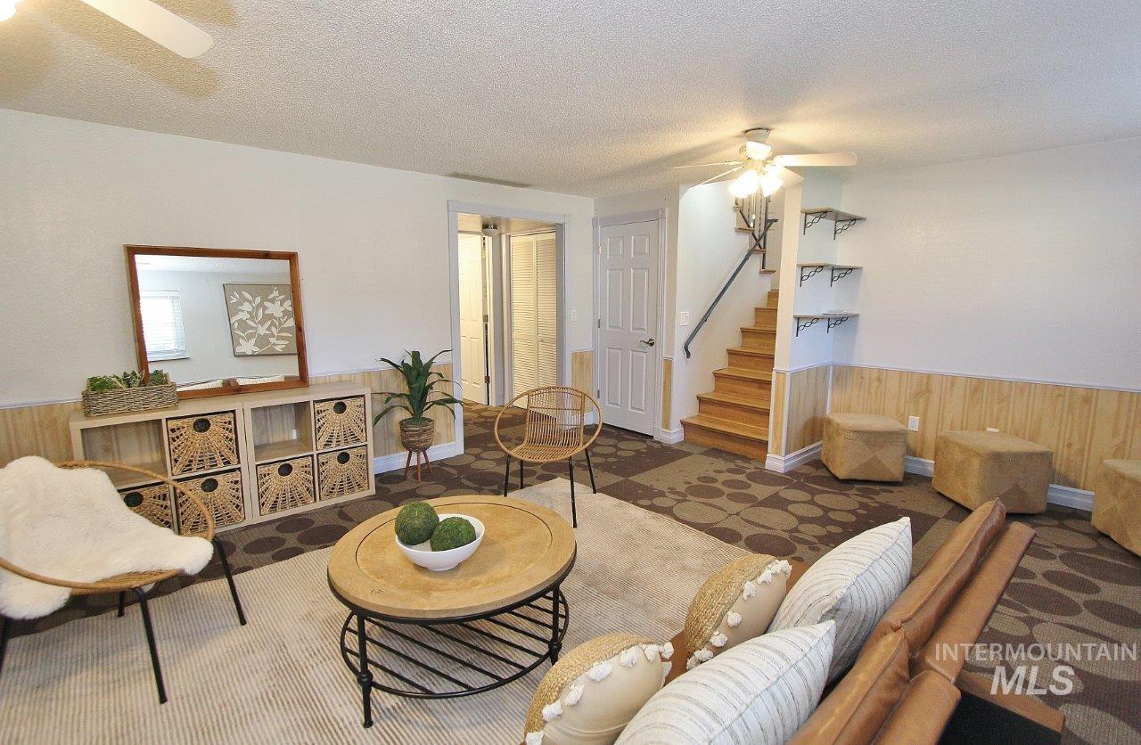 Living room with wood walls, a ceiling fan, wainscoting, a textured ceiling, and stairway
