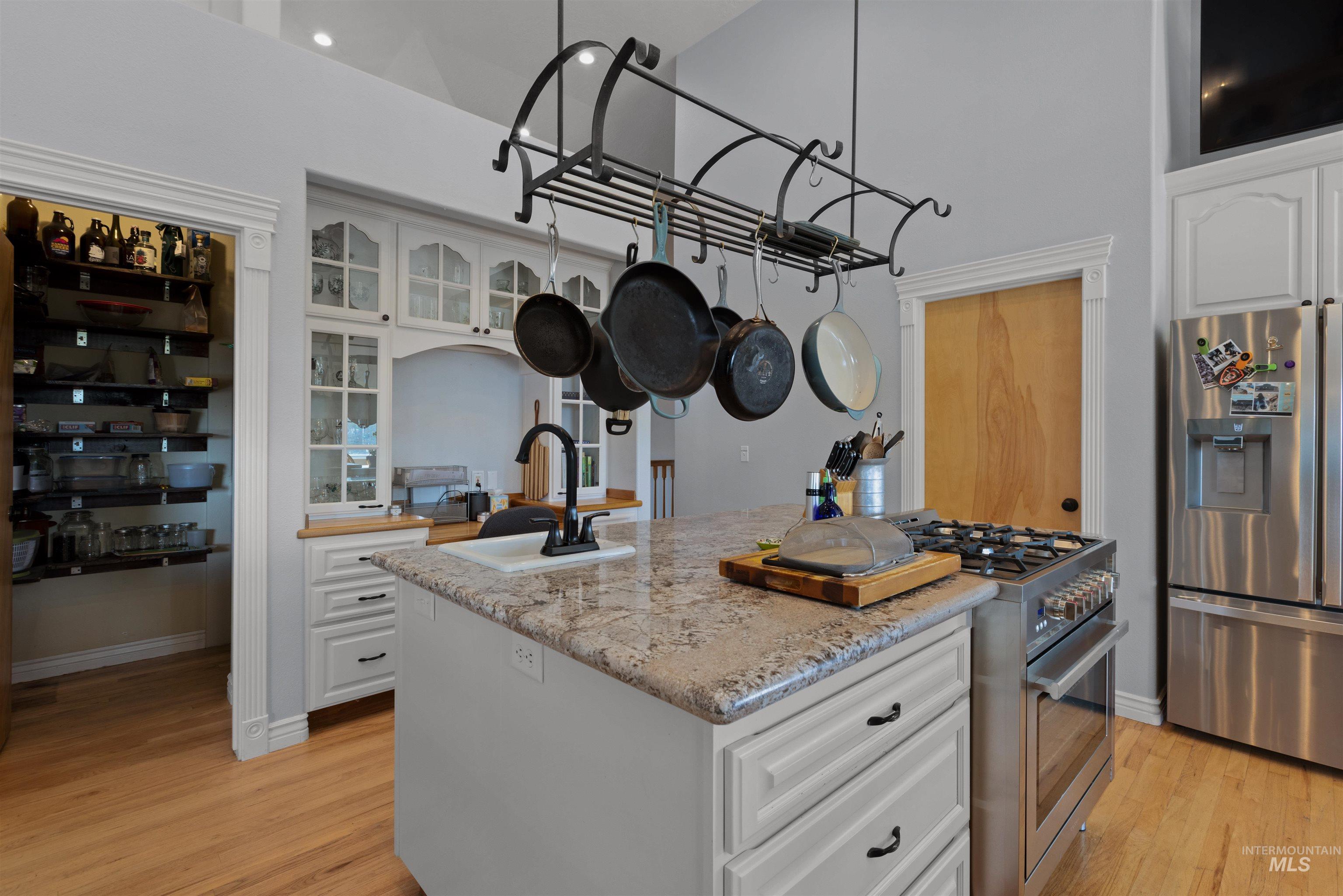 Kitchen featuring white cabinets, appliances with stainless steel finishes, a center island with sink, and light wood finished floors