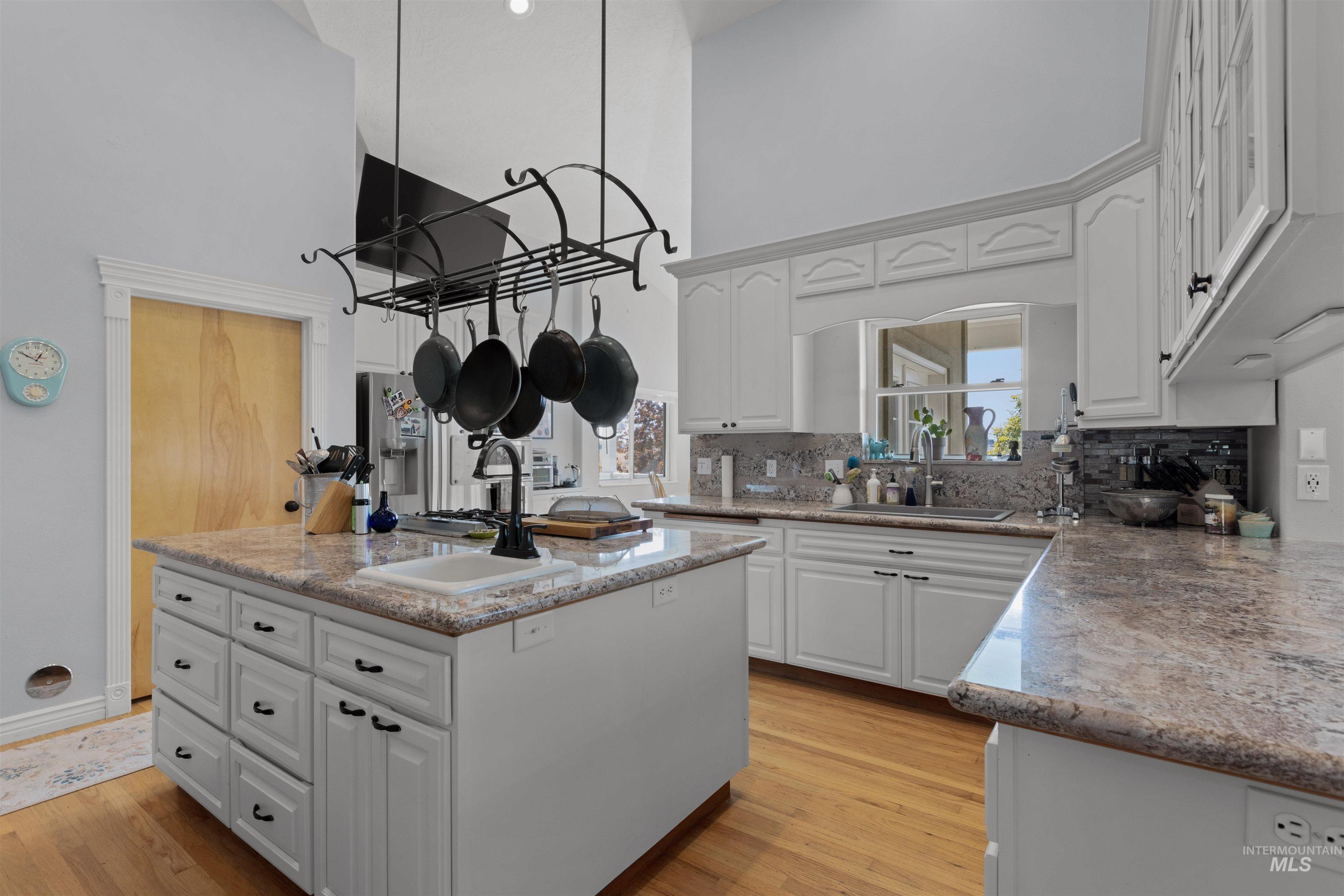 Kitchen with white cabinetry, a high ceiling, light wood-type flooring, an island with sink, and light stone counters