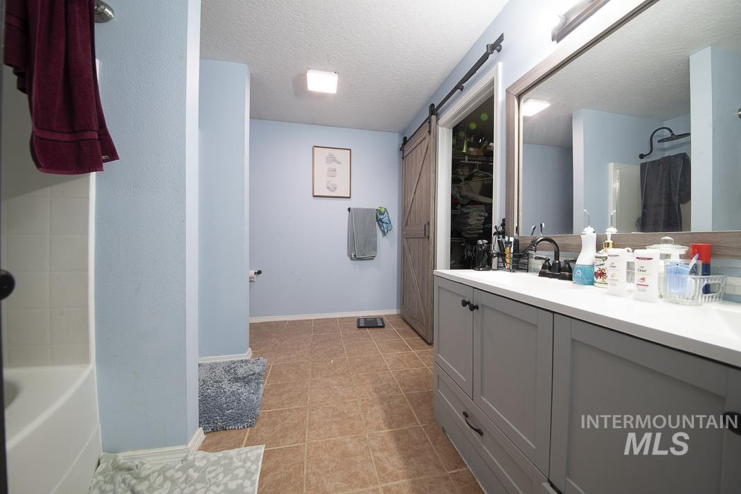 Full bathroom featuring double vanity, a textured ceiling, light tile patterned floors, and shower / bathtub combination