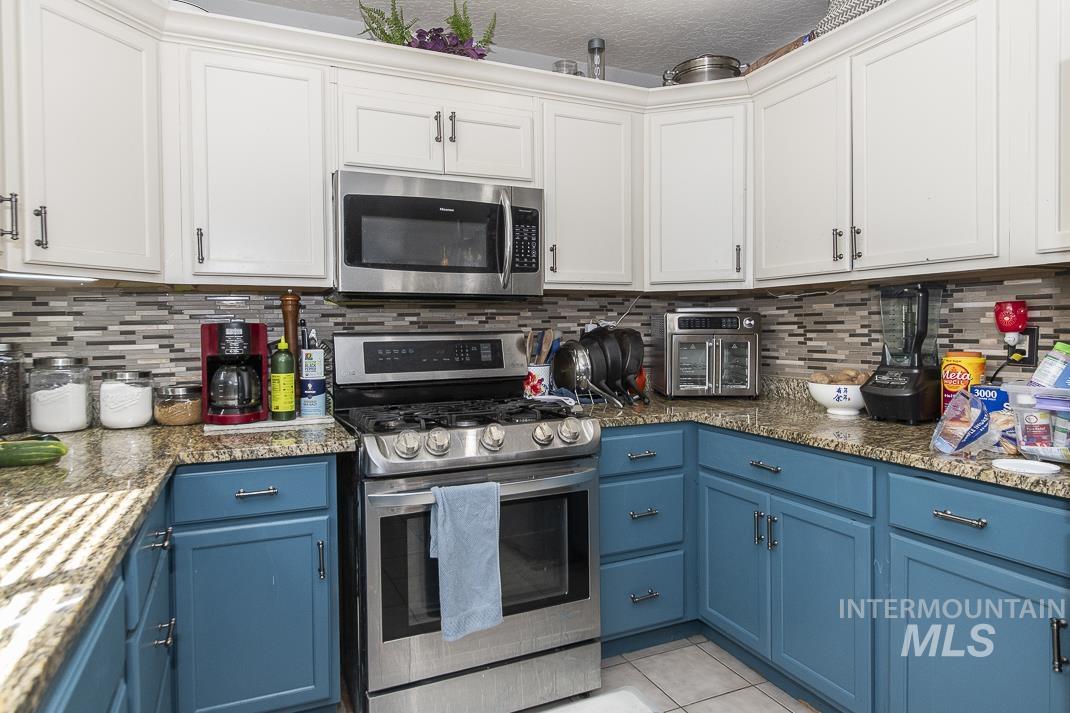Kitchen with blue cabinetry, appliances with stainless steel finishes, backsplash, light tile patterned floors, and a textured ceiling