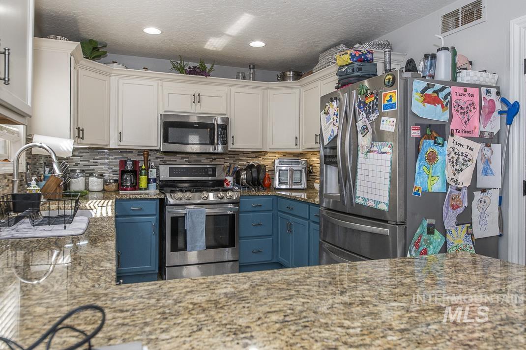 Kitchen featuring dark stone countertops, appliances with stainless steel finishes, a textured ceiling, backsplash, and blue cabinetry