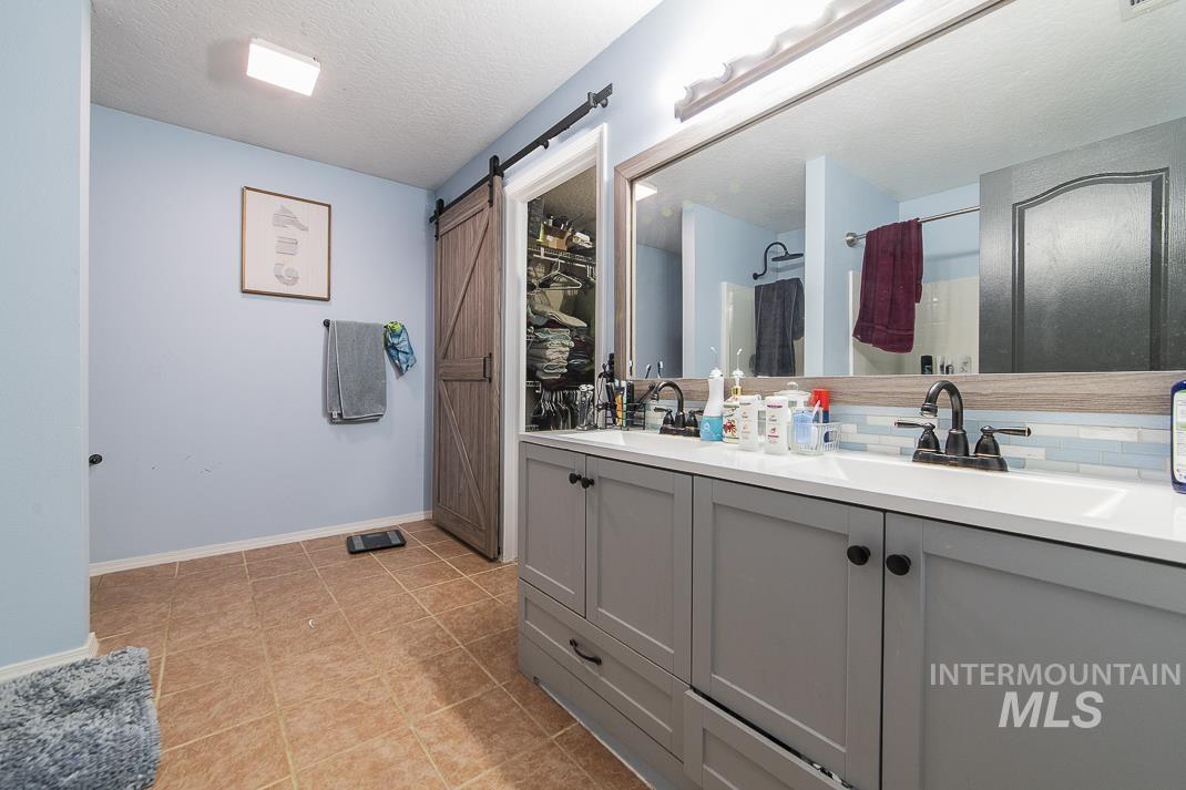 Bathroom featuring a shower with curtain, double vanity, a textured ceiling, light tile patterned flooring, and a walk in closet
