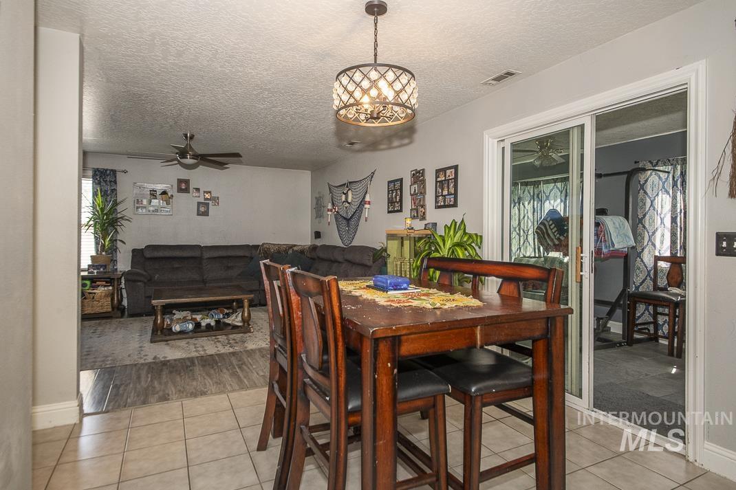 Dining area with ceiling fan, a textured ceiling, light tile patterned flooring, and a chandelier