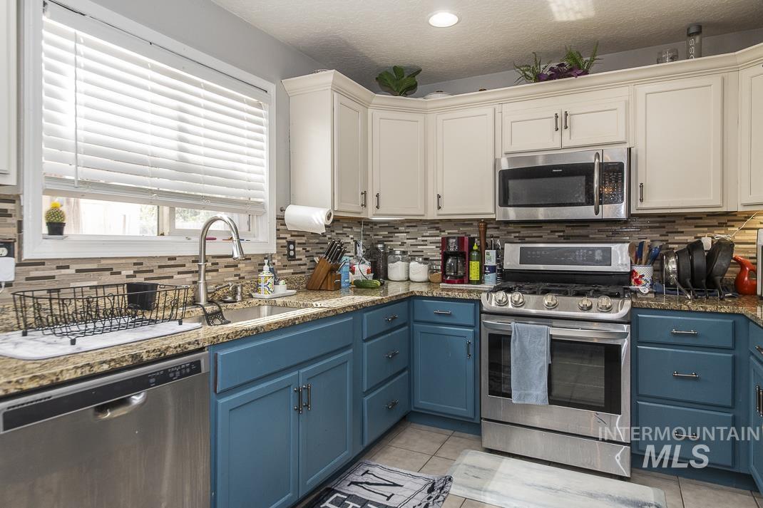 Kitchen featuring blue cabinetry, stainless steel appliances, decorative backsplash, light tile patterned floors, and a textured ceiling