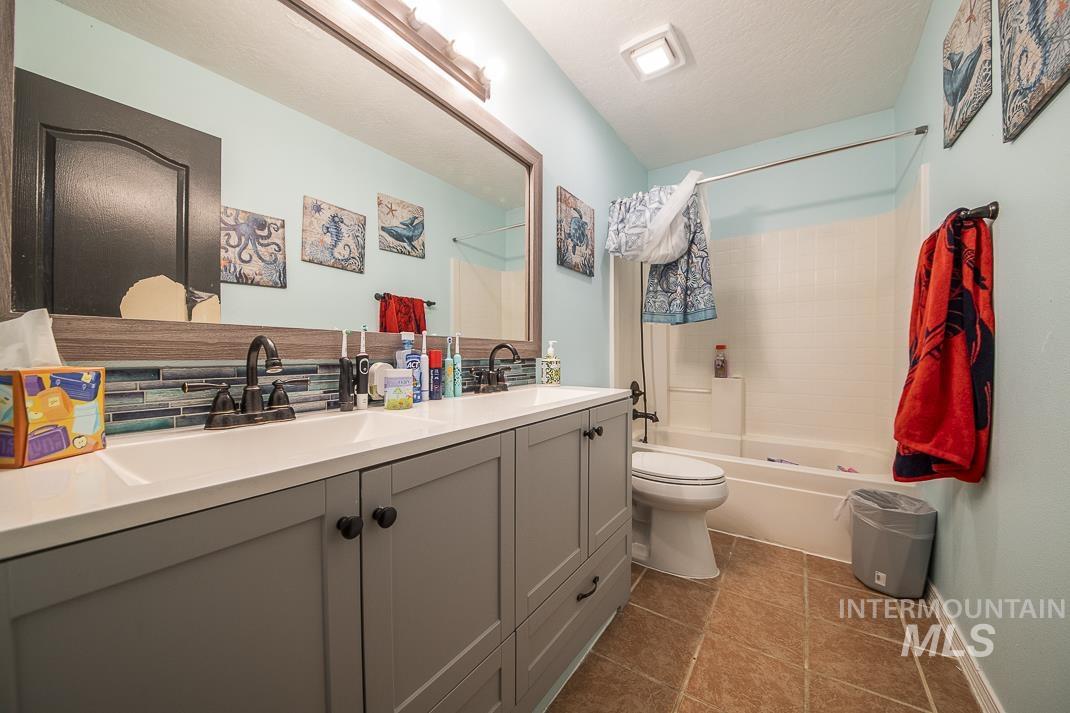 Bathroom with shower / tub combo with curtain, double vanity, dark tile patterned floors, and a textured ceiling