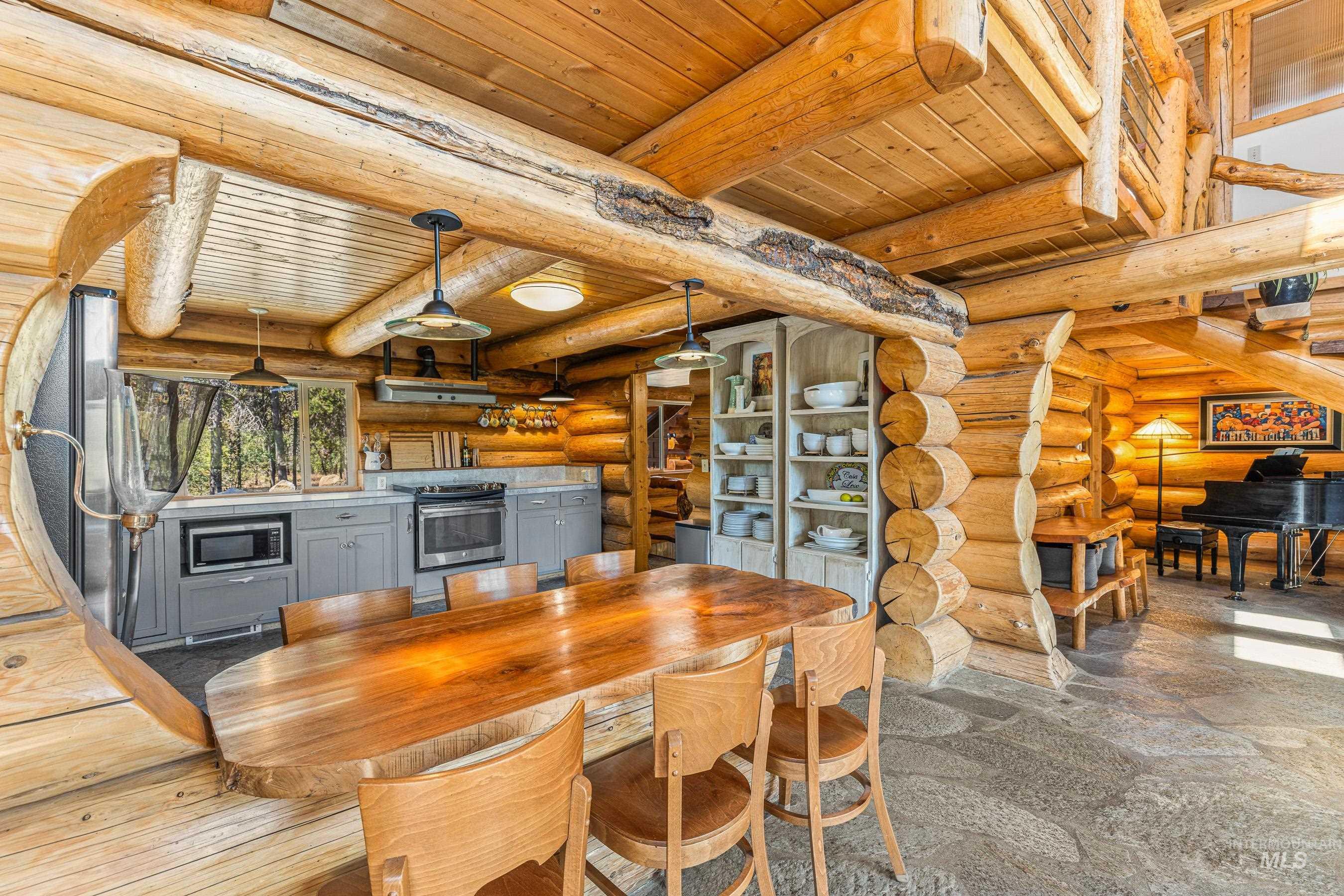 Dining room with a wood ceiling with exposed beams, log walls, and dark stone finish floors
