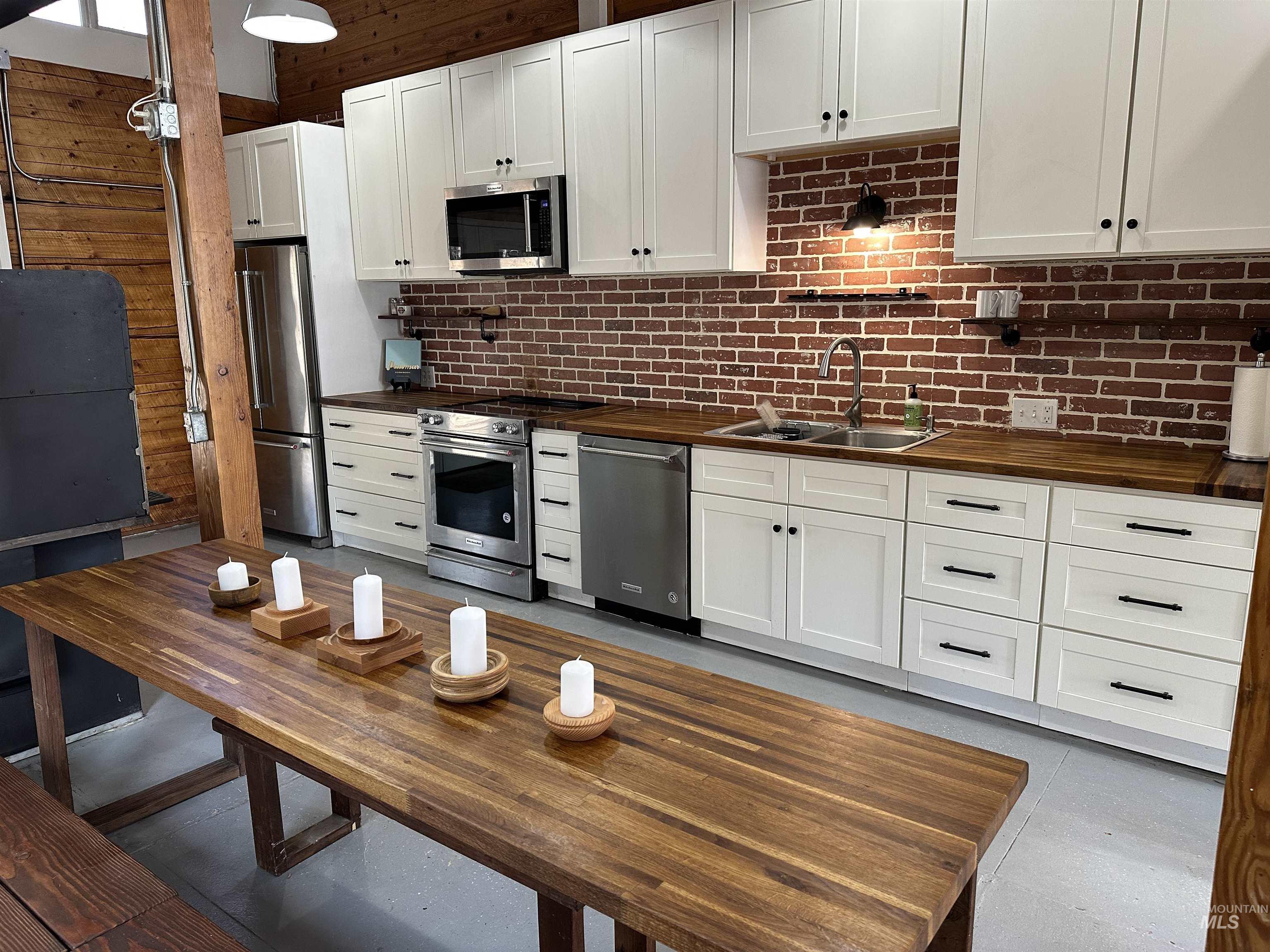 Kitchen with stainless steel appliances, white cabinetry, decorative backsplash, and butcher block counters